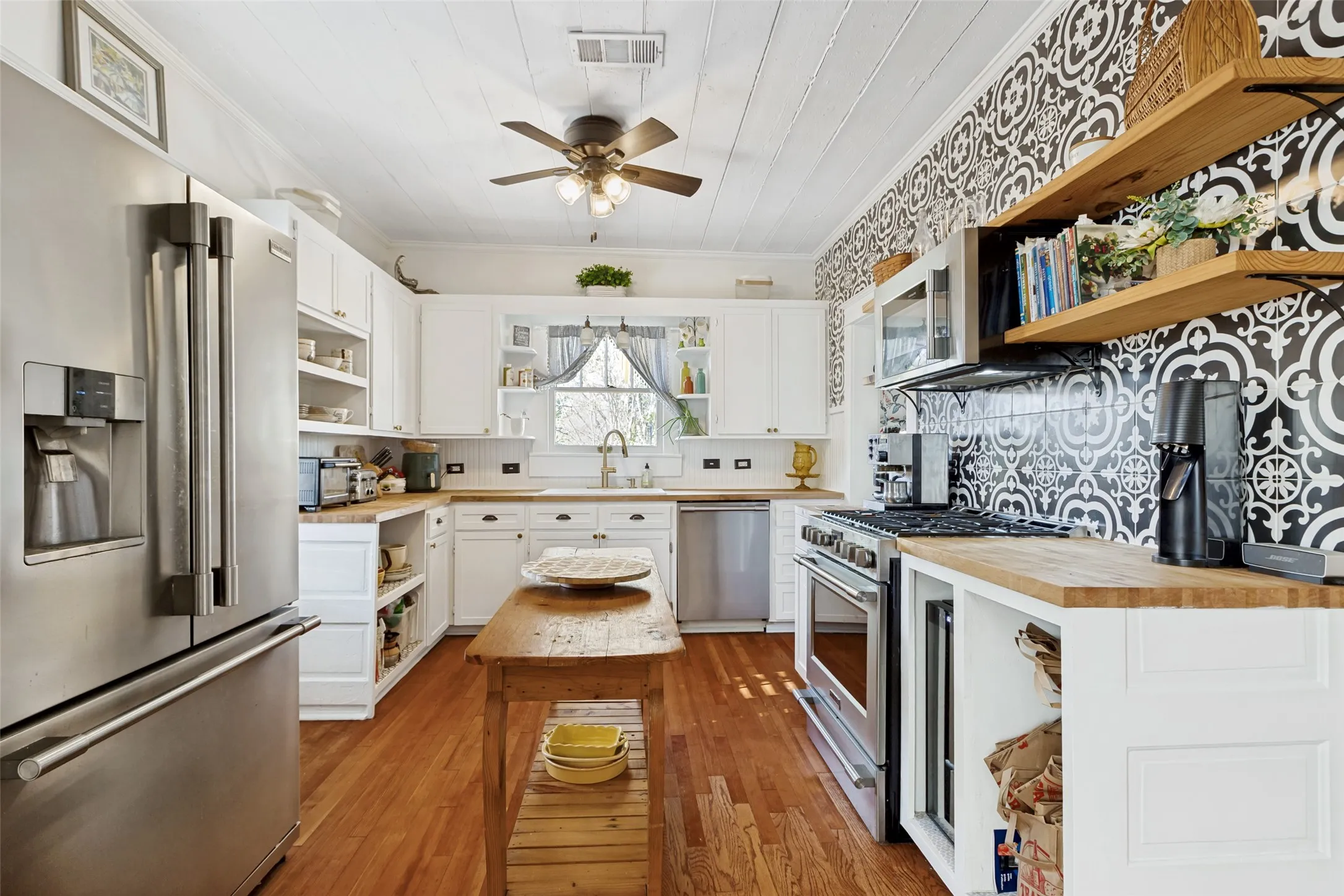 Kitchen featuring wood-finish flooring, white cabinetry, stainless steel appliances, and a decorative tile backsplash