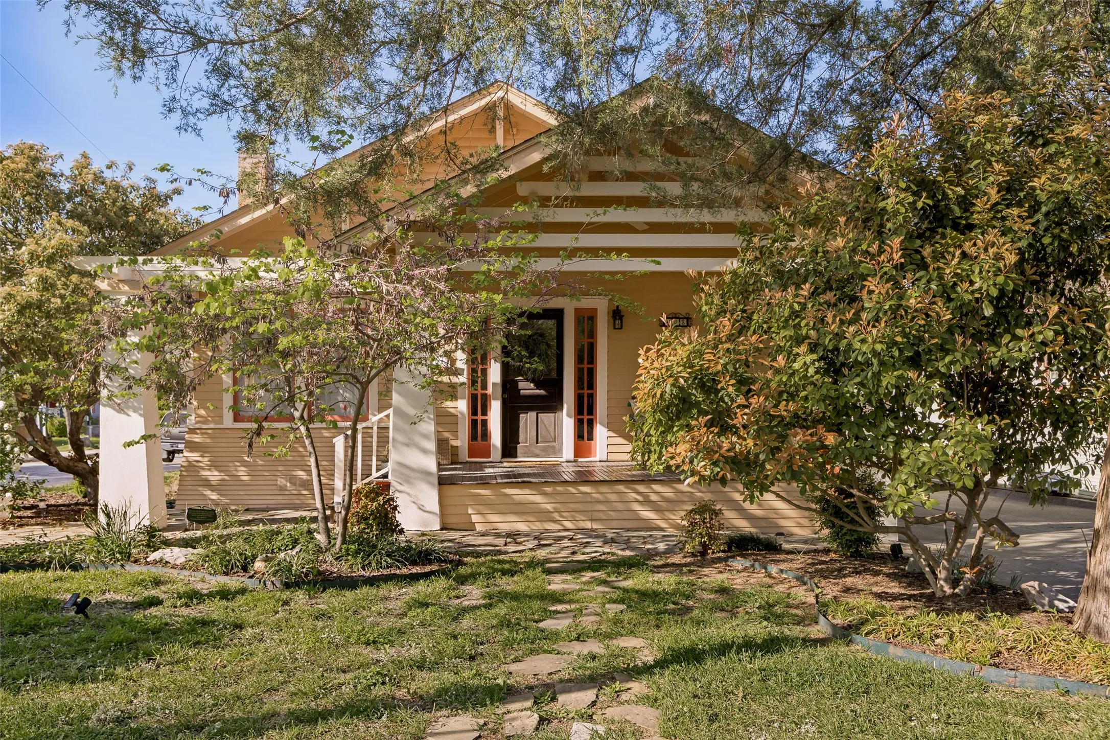 Single-story residence featuring a covered front porch with white pillars, a natural wood paneled front door, and a prominent chimney