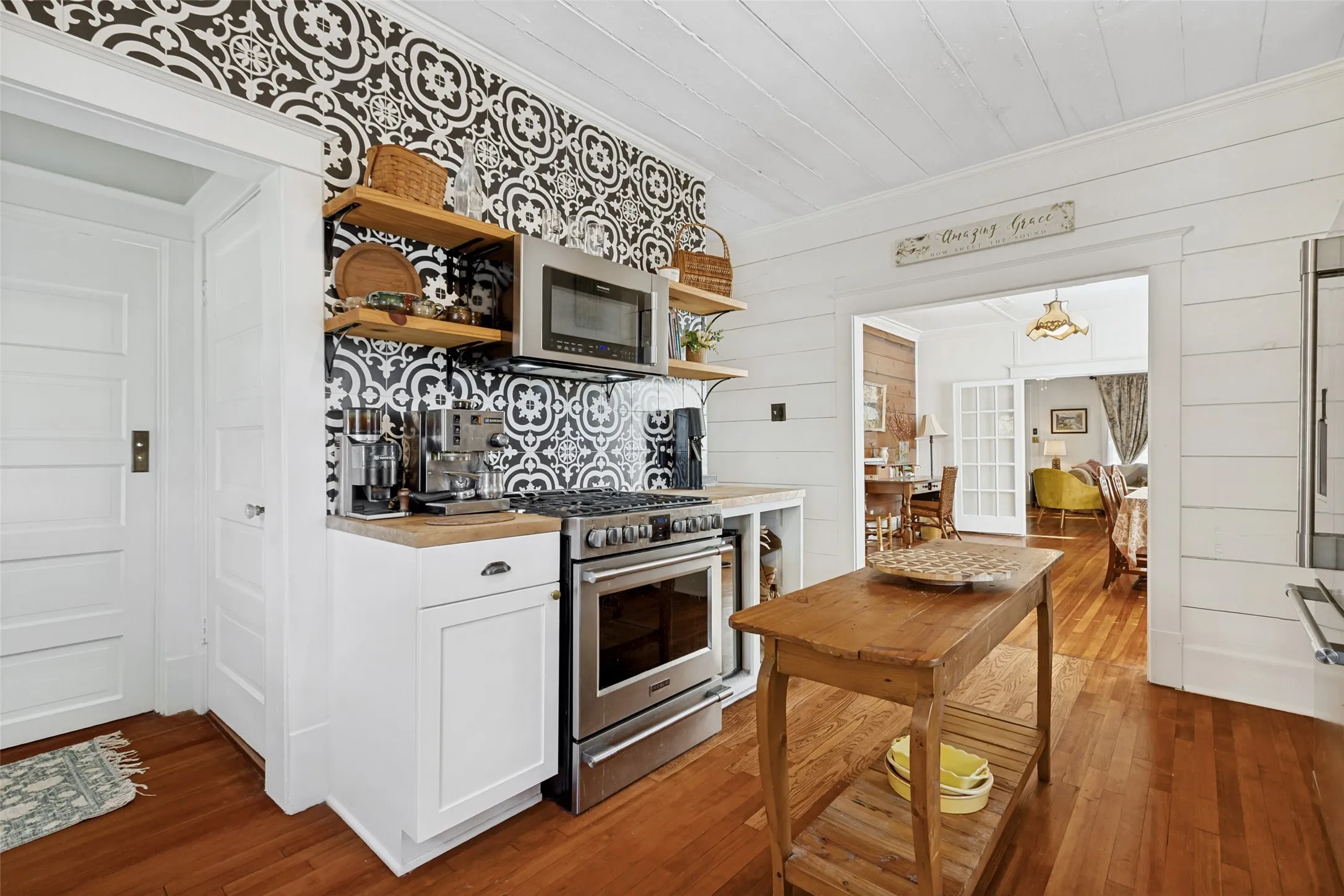 Hardwood flooring throughout, white paneled walls, white shaker-style cabinetry, patterned tile backsplash, and stainless steel appliances