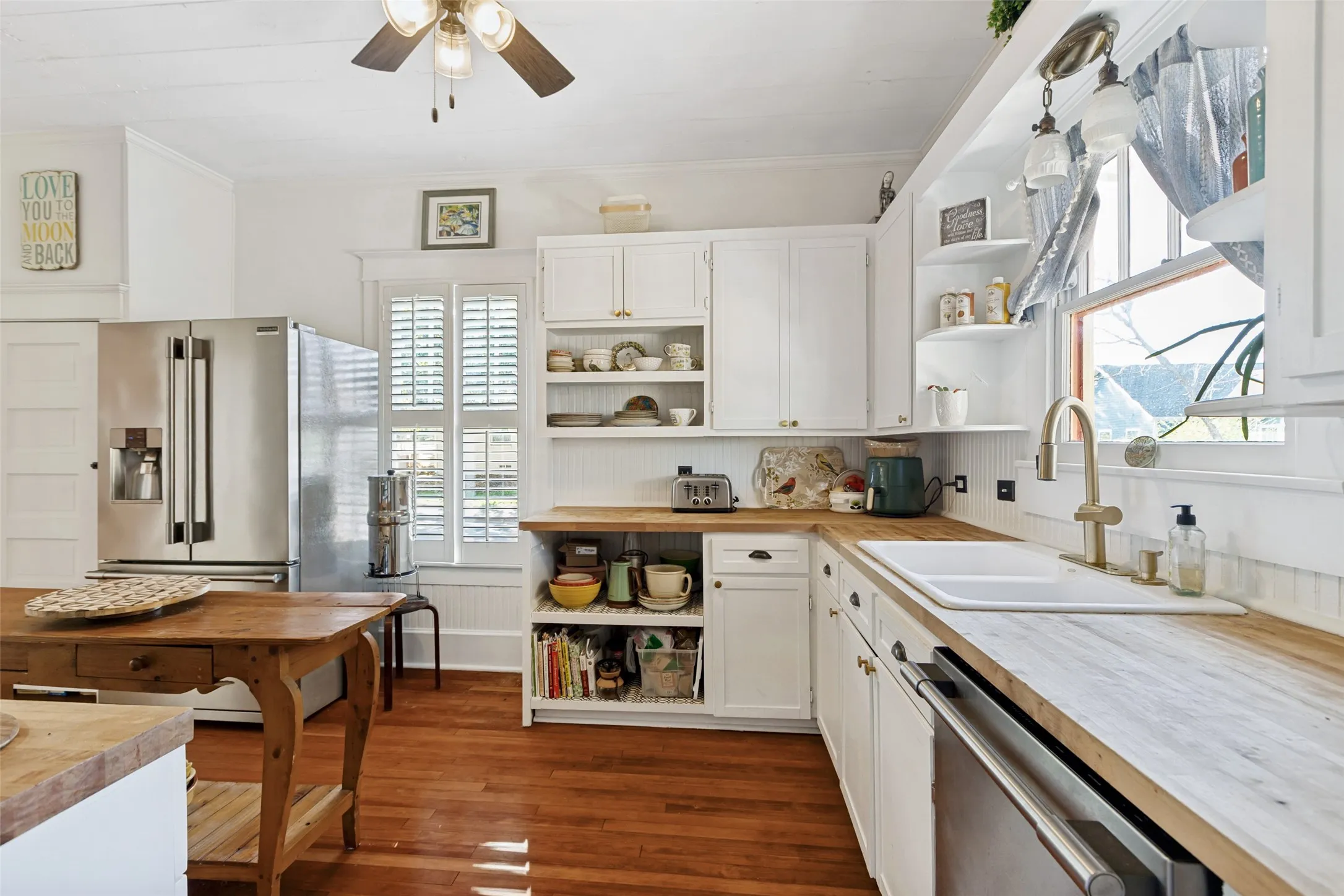 Wood-finish flooring, white cabinetry with gold-tone hardware, wood-finish countertops, stainless steel refrigerator, and recessed sink with a gold-tone faucet