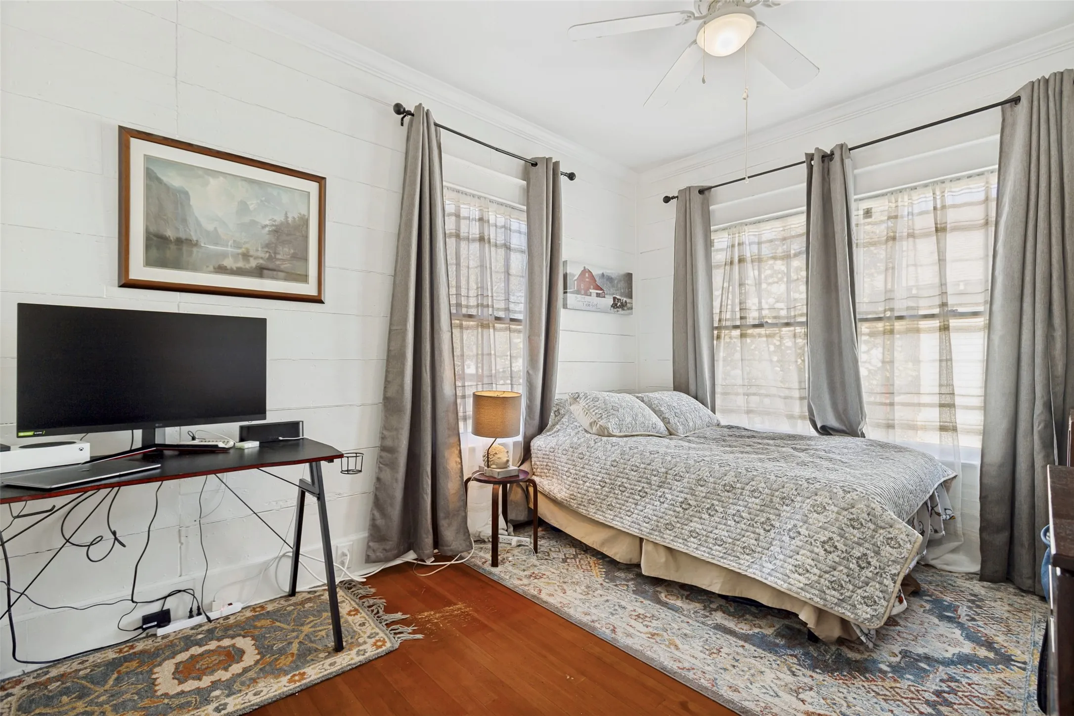 Hardwood flooring, white shiplap wall accent, white ceiling fan with integrated lighting, and multiple windows