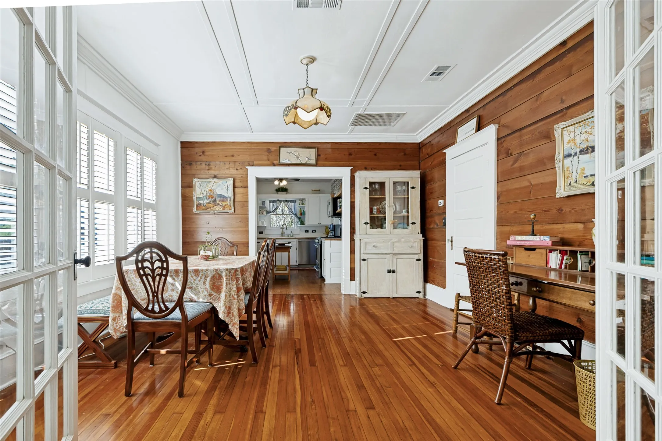 Hardwood flooring, wood paneling, white built-in hutch, white plantation shutters, and white French doors