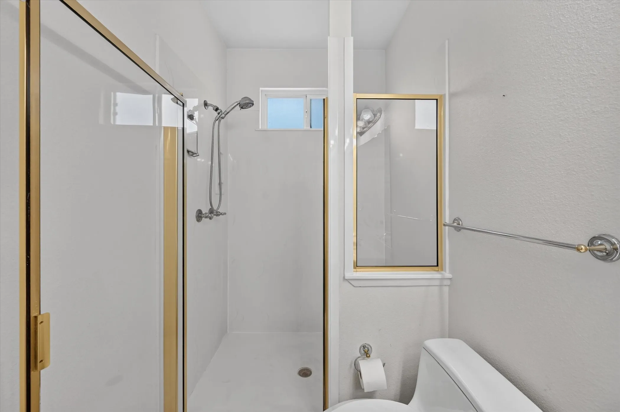 Walk-in shower with gold-tone framed glass enclosure and integrated shower system