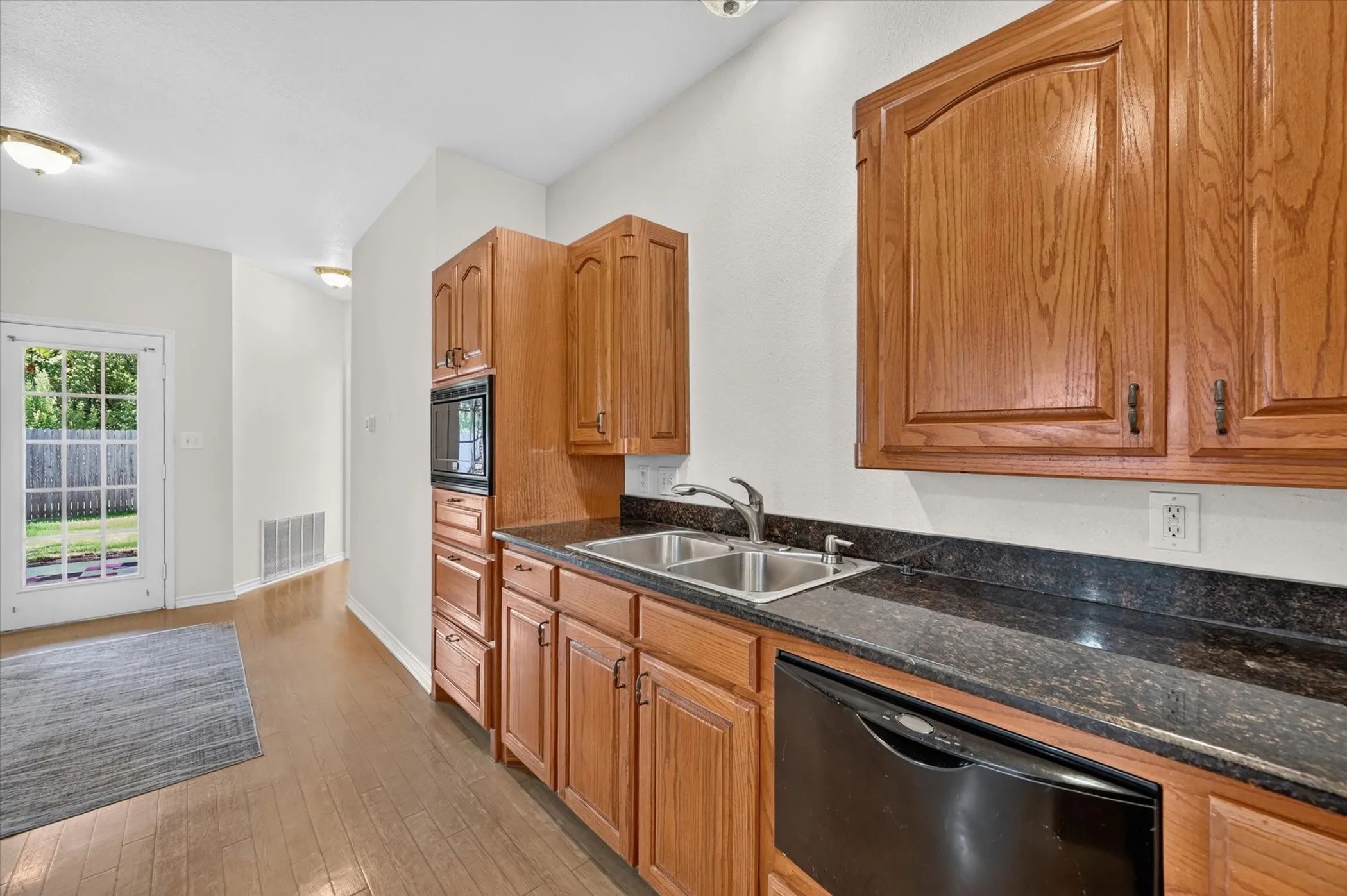 Light wood-finish flooring, wood cabinetry, built-in microwave, dual basin sink, and black appliance
