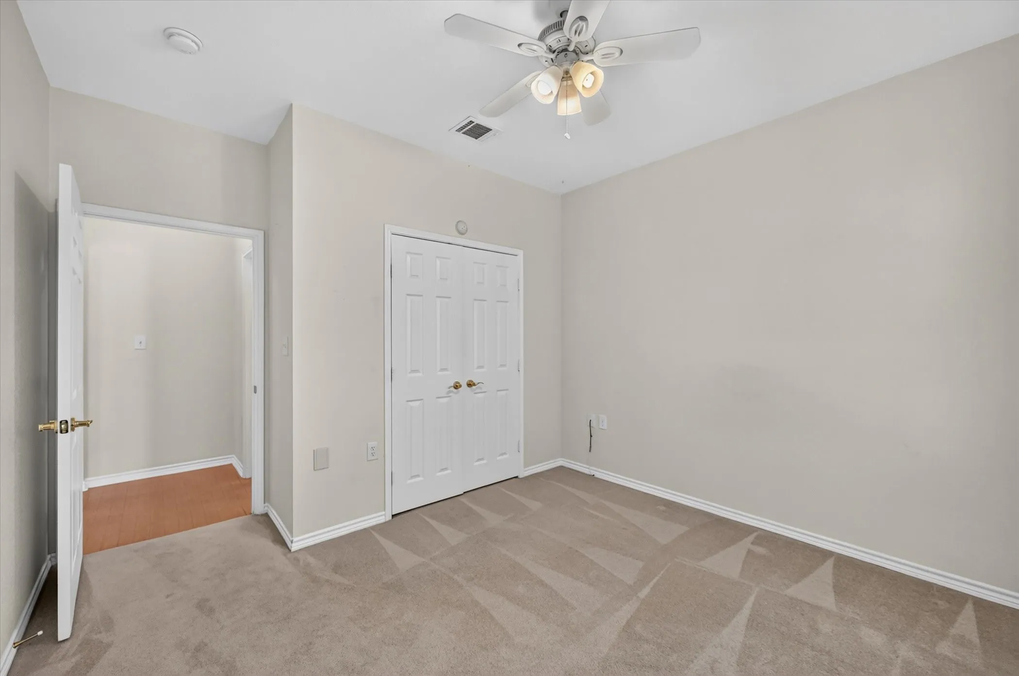 Spacious bedroom with neutral wall finishes, wood-finish flooring, dual closets with white six-panel doors, and a ceiling fan with integrated lighting fixture