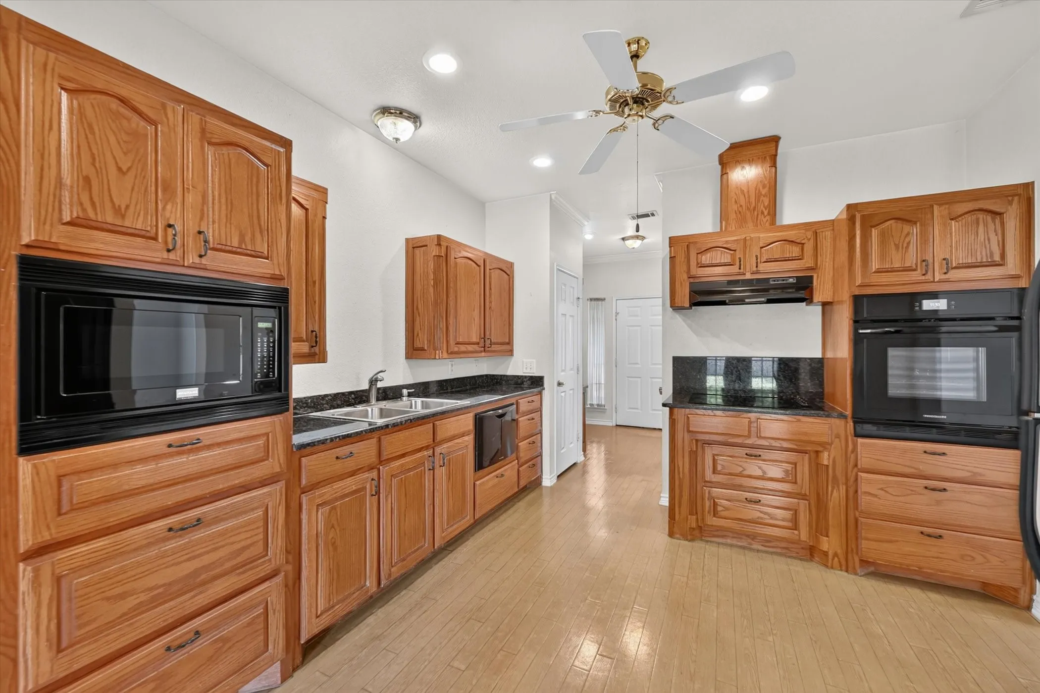 Wood-finish flooring with extensive cabinetry, dark stone countertops, and integrated black appliances