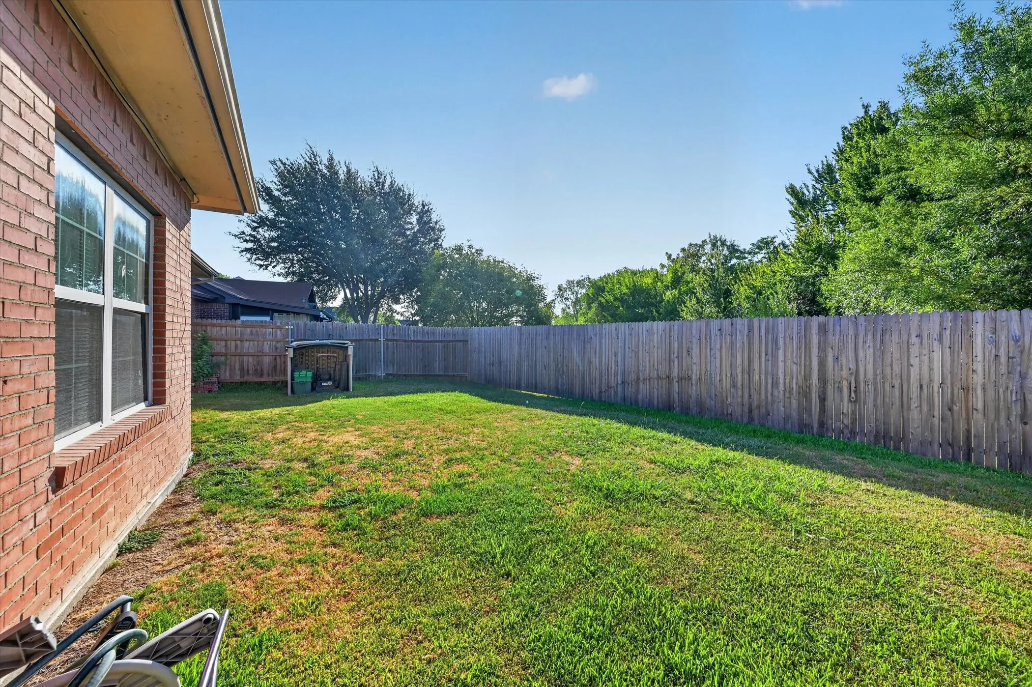 Expansive backyard with a full-height wood privacy fence, brick exterior, and multiple windows