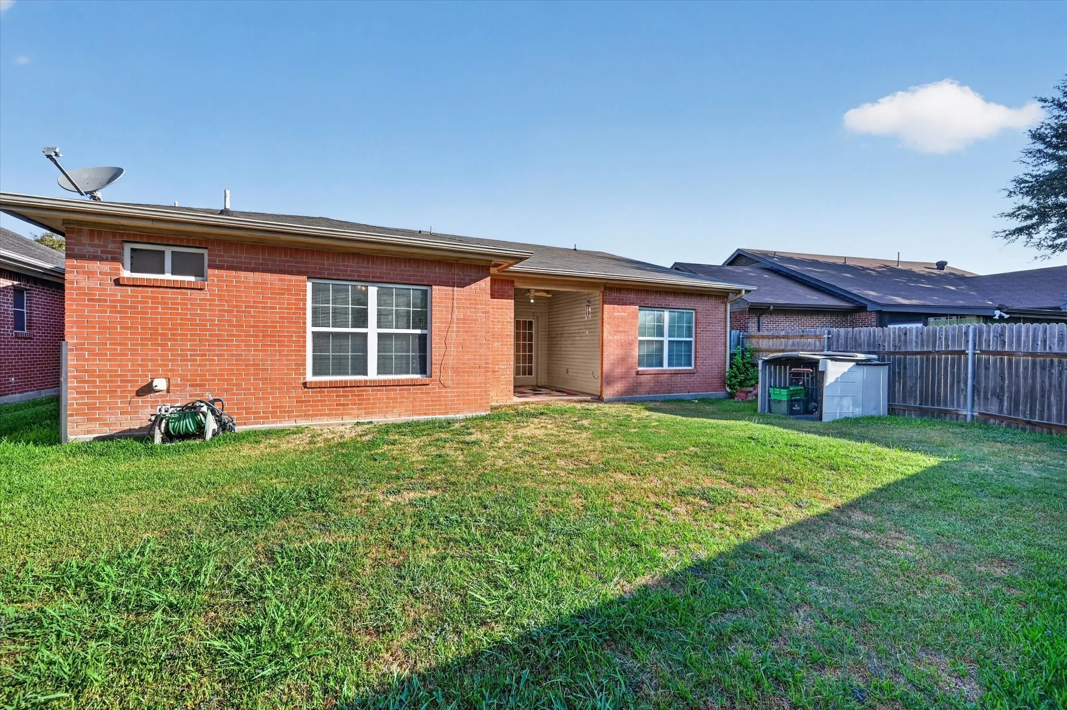 Expansive grassy area with a brick exterior, white-framed windows, and a wood privacy fence