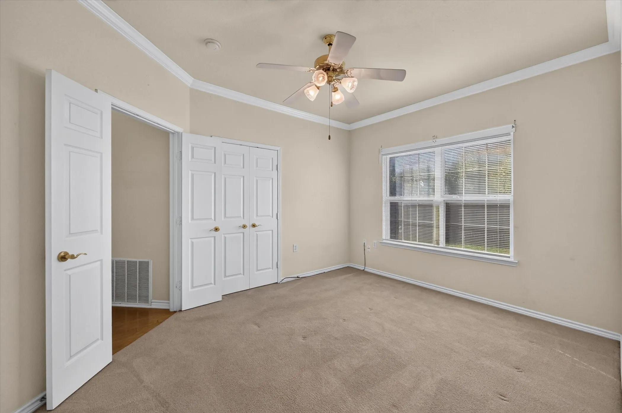 Crown molding, ceiling fan with integrated lighting, window with blinds, bi-fold closet doors, and a paneled entry door