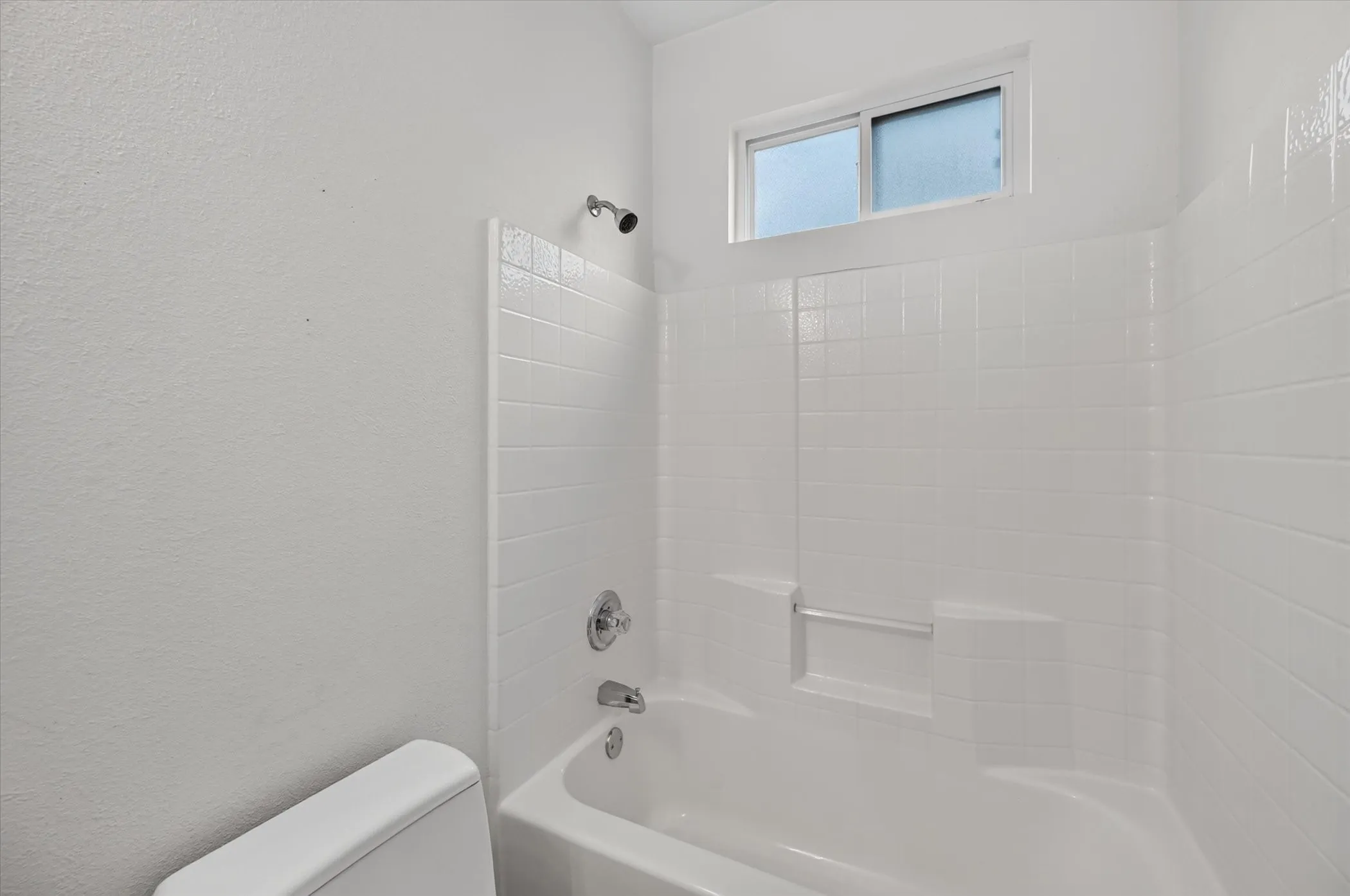 White bathtub with an integrated shower, chrome fixtures, and a high-set window
