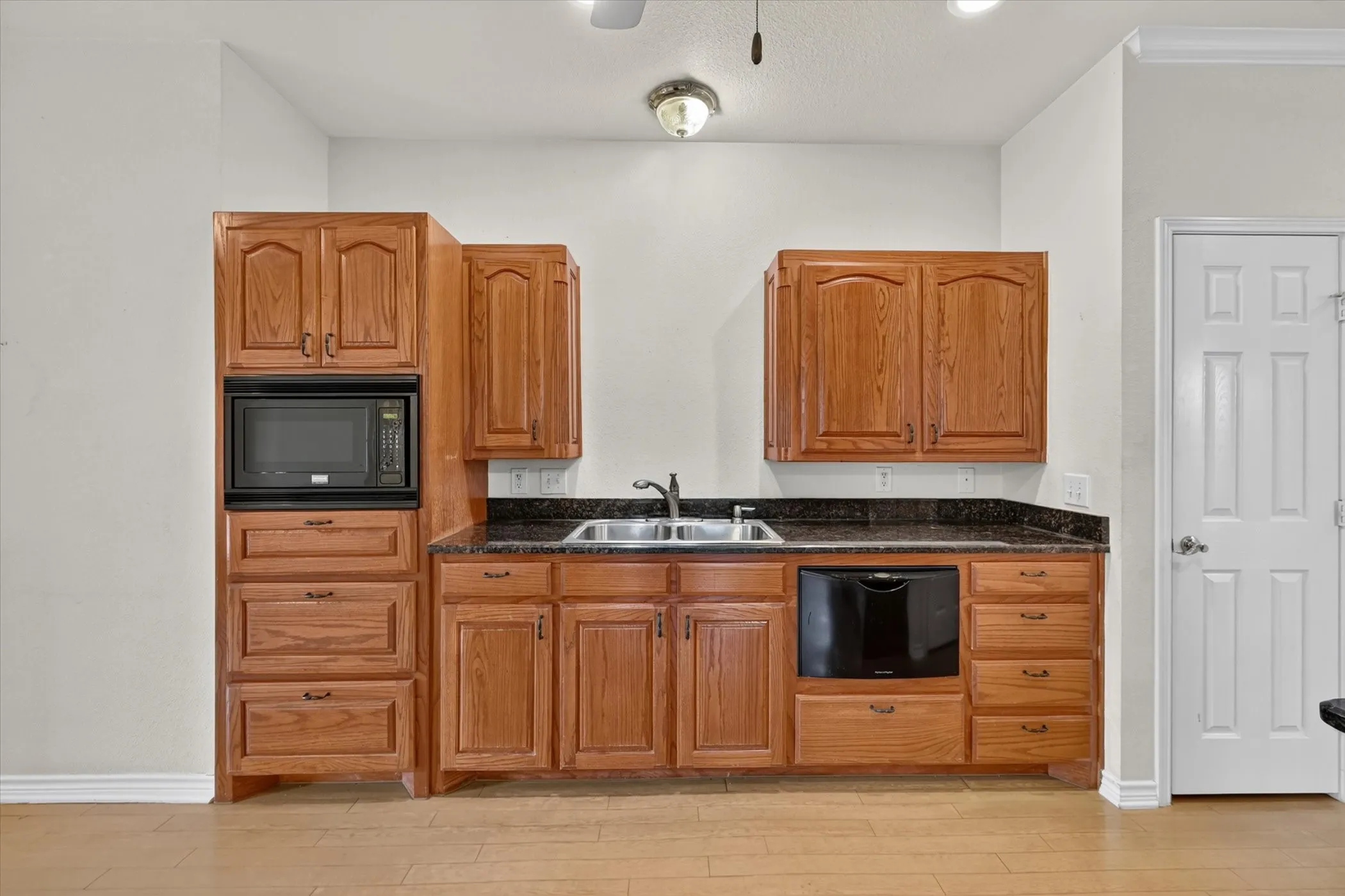 Wood-finish flooring, built-in microwave, integrated dishwasher, double basin sink, and wood cabinetry