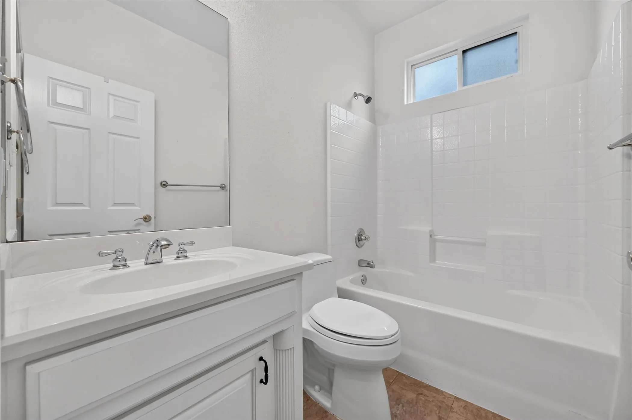 White vanity with an integrated sink and chrome faucet, white paneled door, built-in bathtub with white subway tile surround, and a transom window