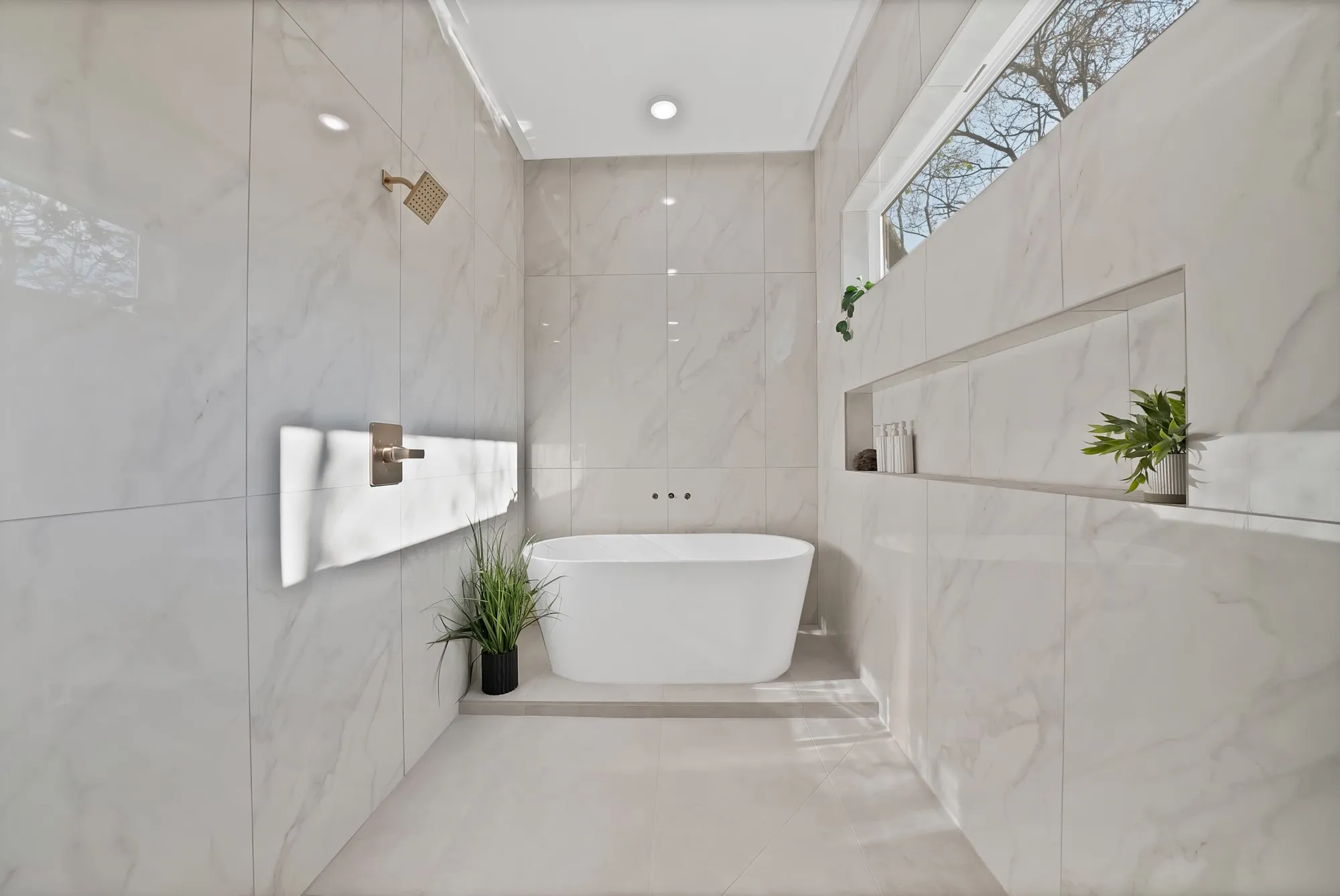 Freestanding soaking tub, large format wall and floor tiling, recessed shelving, and a high window
