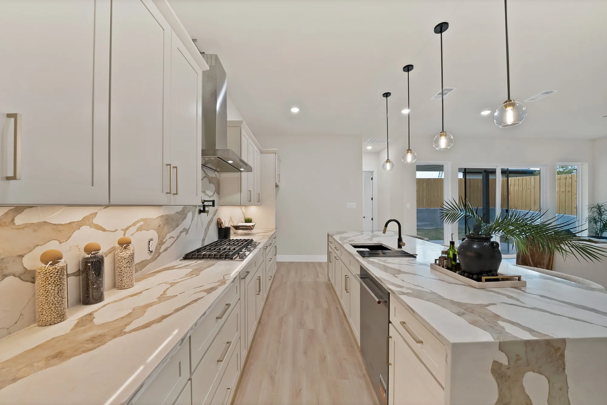 Gourmet kitchen with extensive counter space, custom cabinetry, stainless steel range hood, built-in gas cooktop, and contemporary pendant lighting