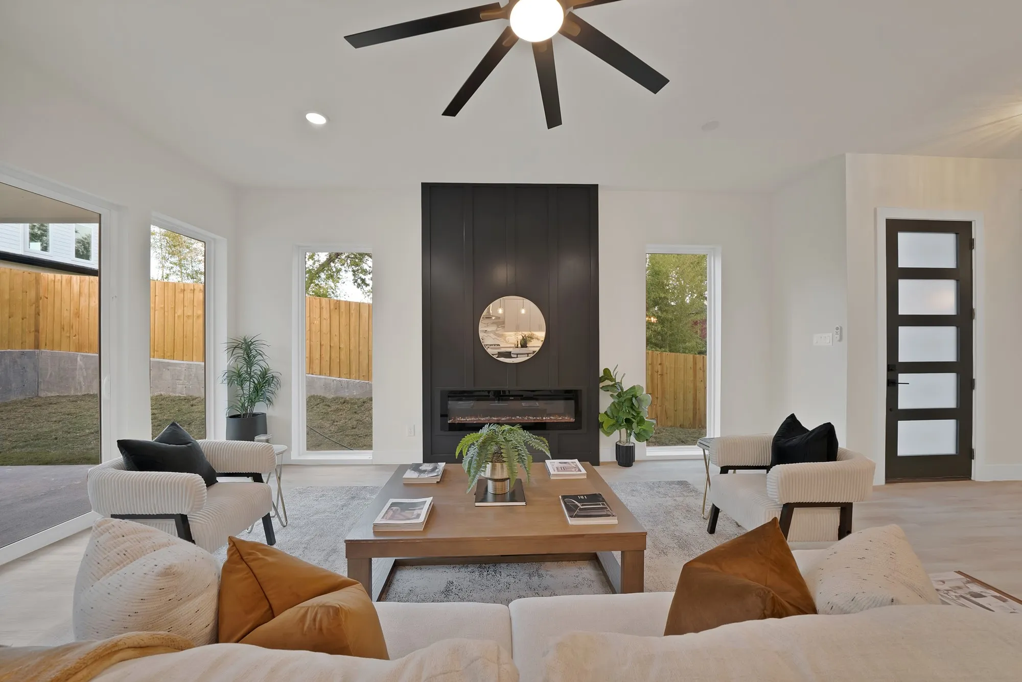 Spacious living area featuring a modern fireplace with a black shiplap surround, light wood-finish flooring, and multiple large windows