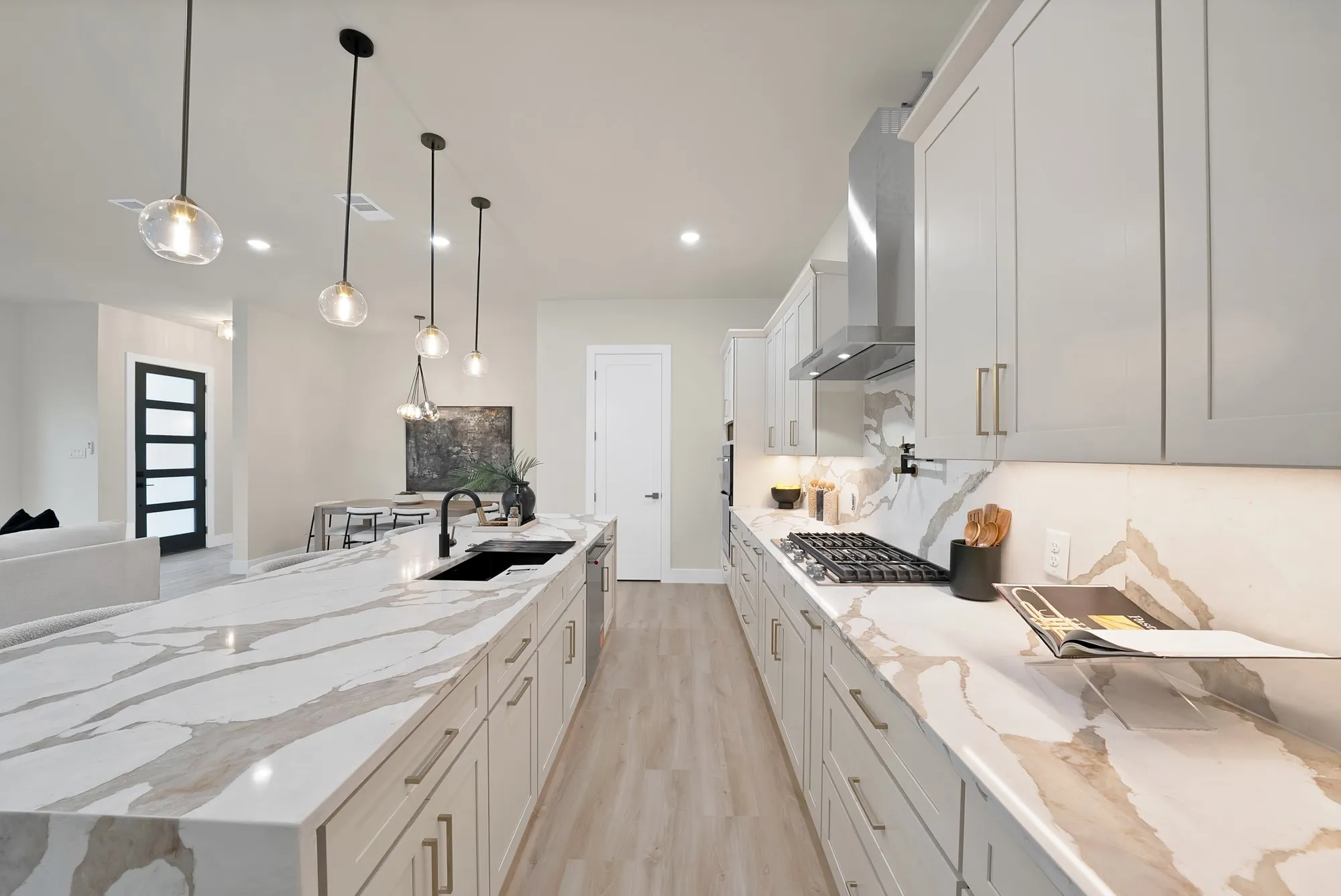 Kitchen featuring a large island, light wood-finish flooring, white cabinetry, integrated sink, and stainless steel appliances