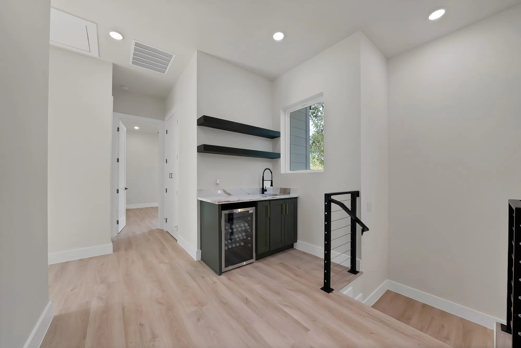 Wood-finish flooring throughout, with a built-in wet bar featuring dark cabinetry, a beverage cooler, and a light-colored countertop