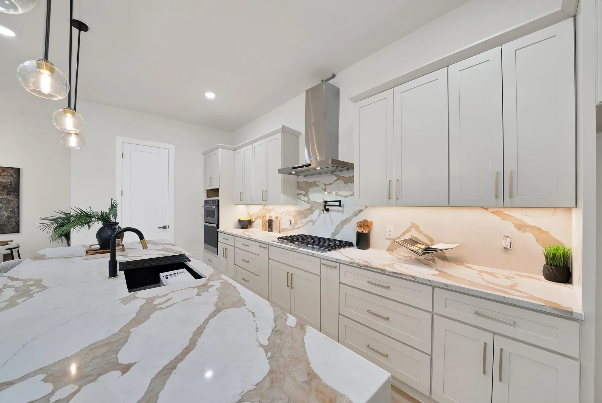 Modern kitchen featuring a large island with an integrated black sink, light cabinetry with brushed nickel hardware, and an expansive countertop with distinct veining