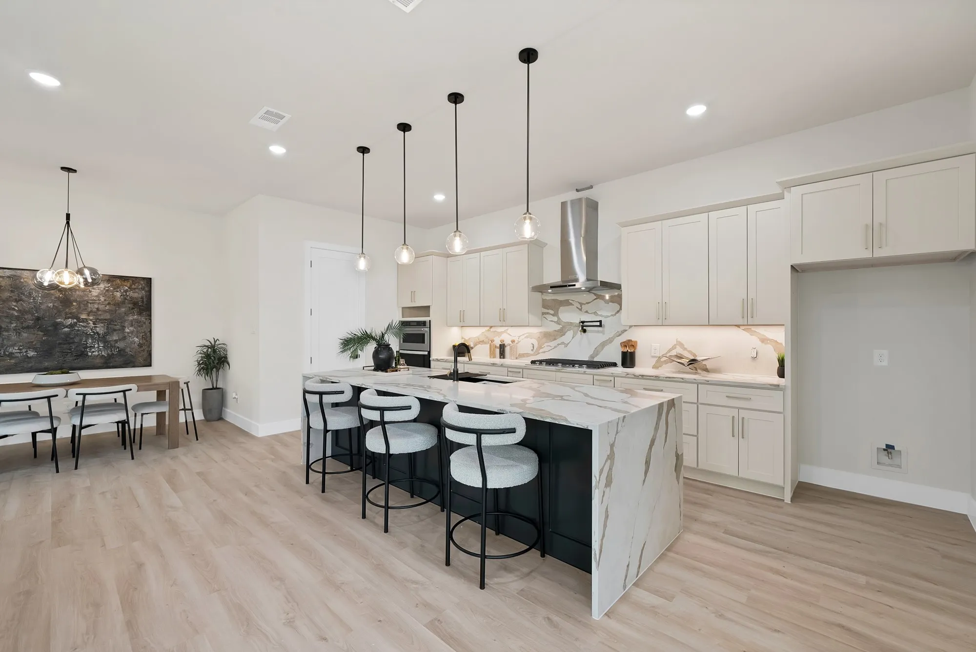 Kitchen with a waterfall-edge island, light-toned wood-finish flooring, built-in stainless steel oven, and a stainless steel range hood