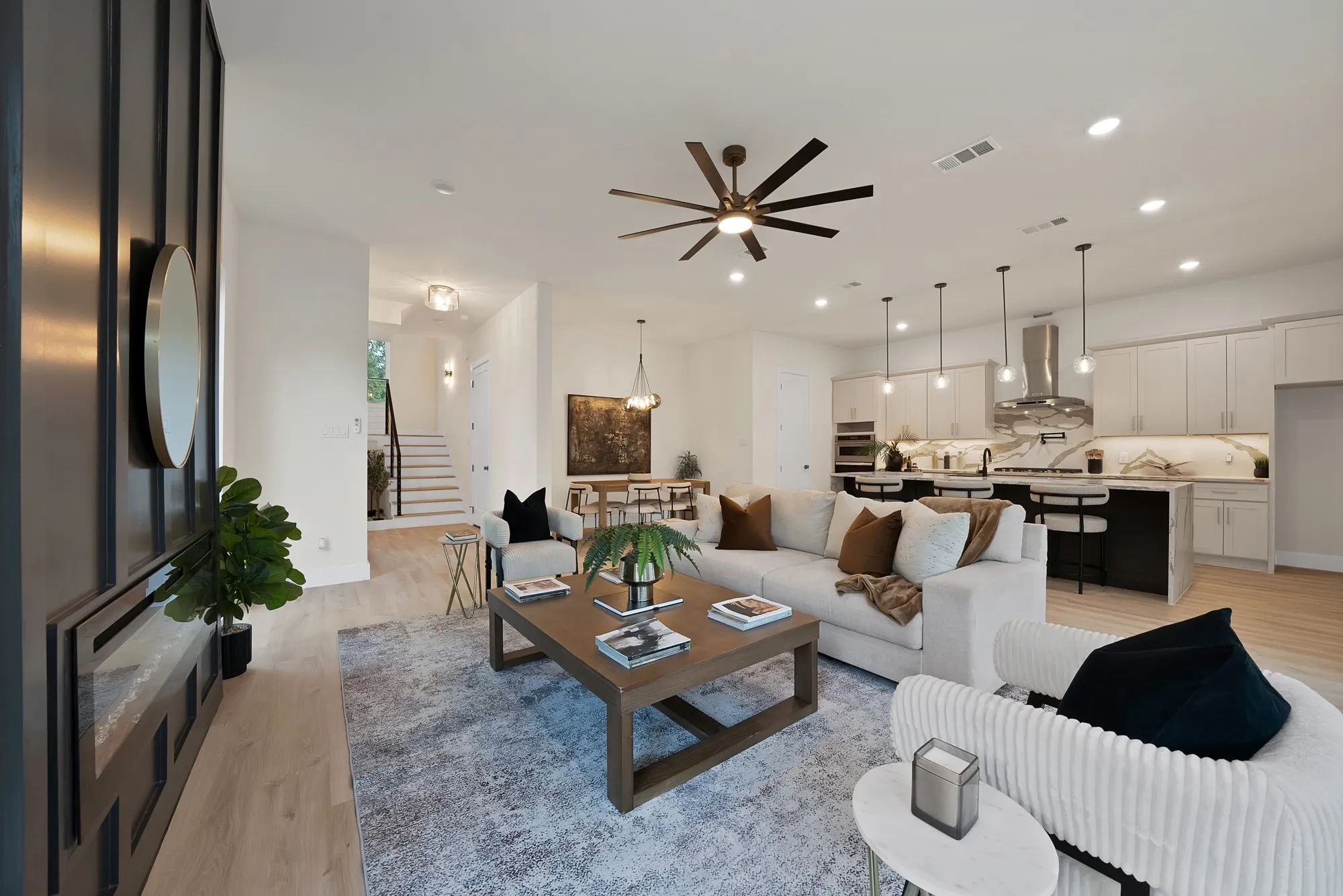 Open-concept living area featuring wood-finish flooring, a contemporary kitchen with a large island, stainless steel appliances, and pendant lighting