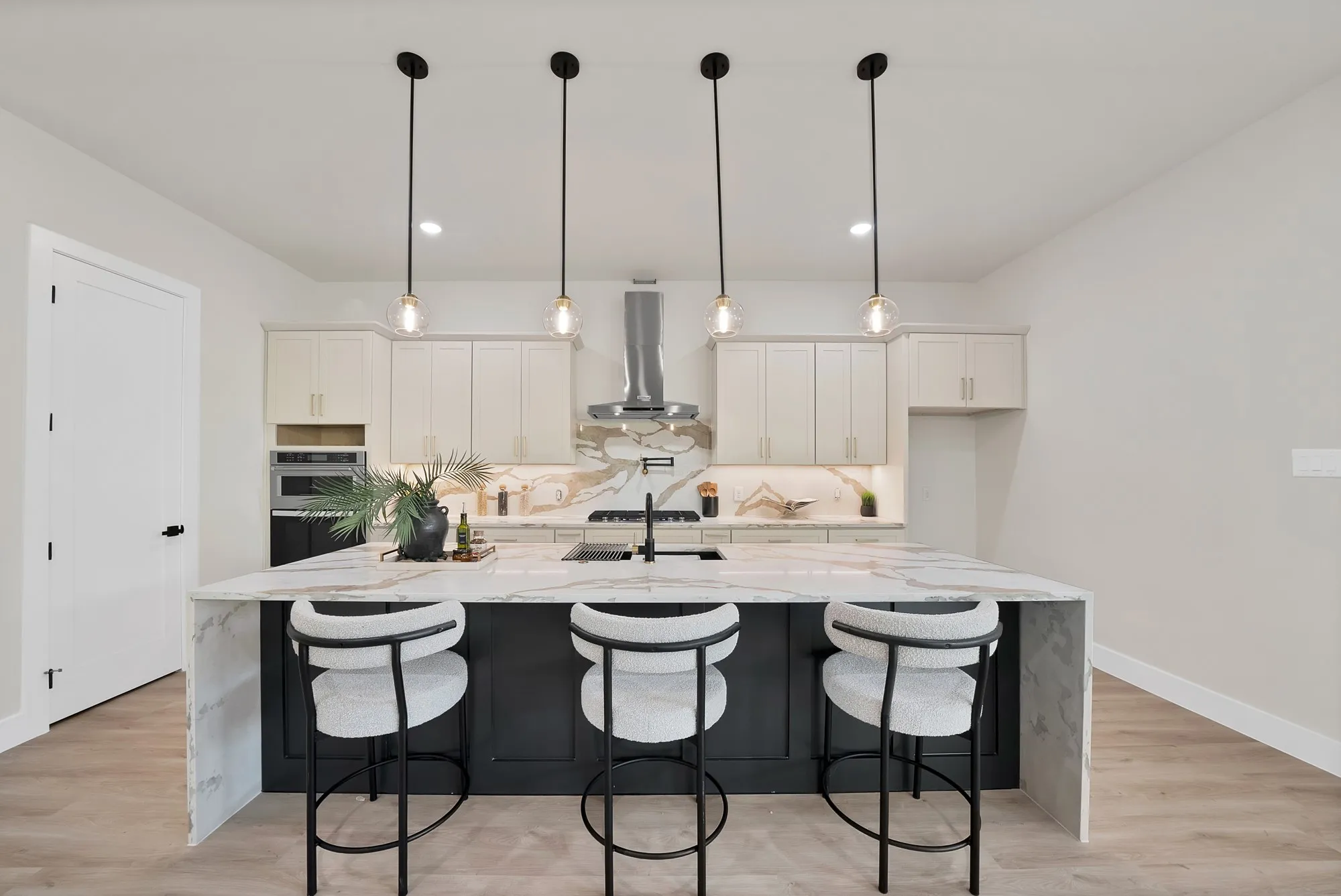 Kitchen featuring a waterfall island, pendant lighting, built-in microwave, stainless steel range hood, and light-toned cabinetry