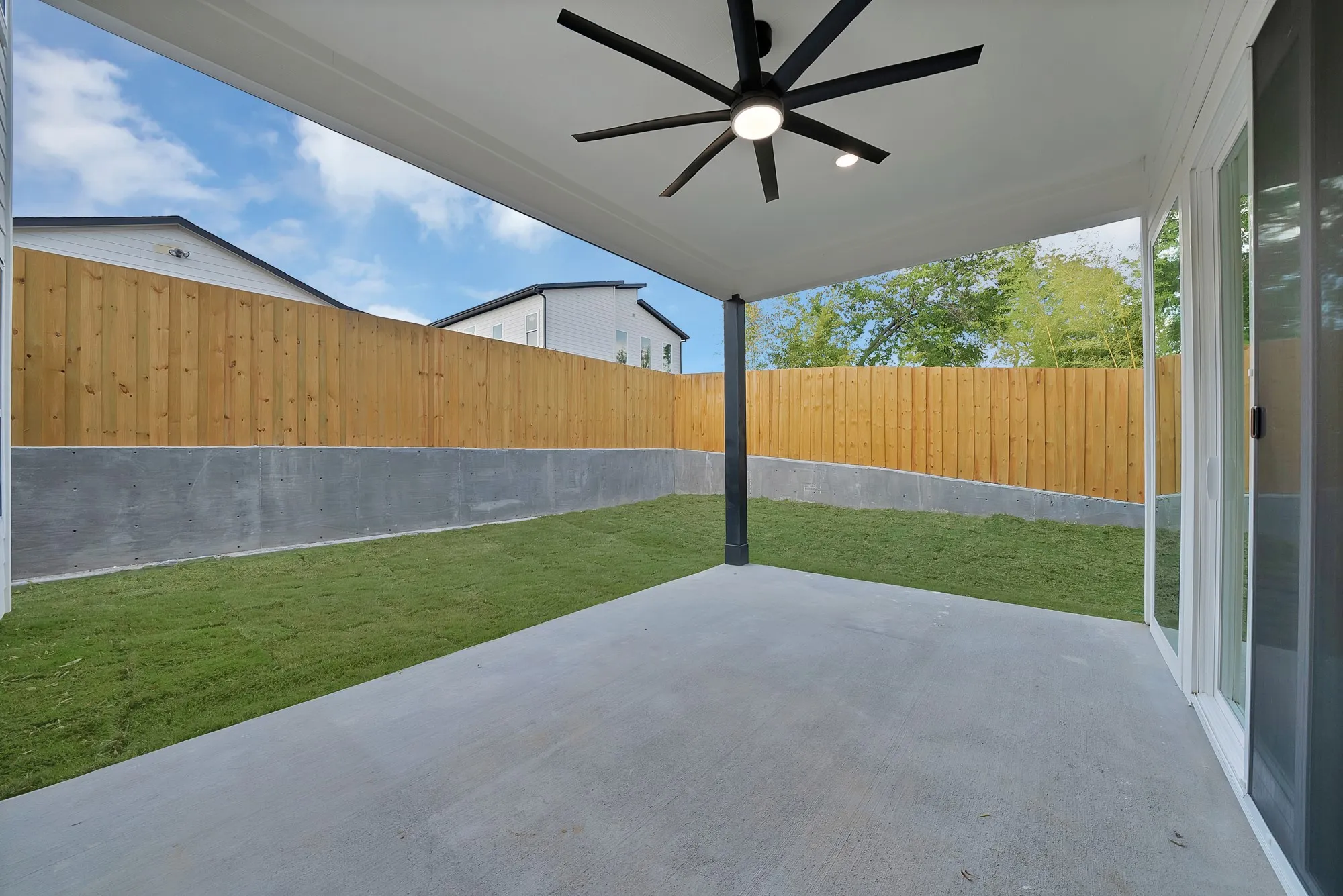 Covered patio featuring a ceiling fan with integrated lighting, concrete flooring, and a grass area