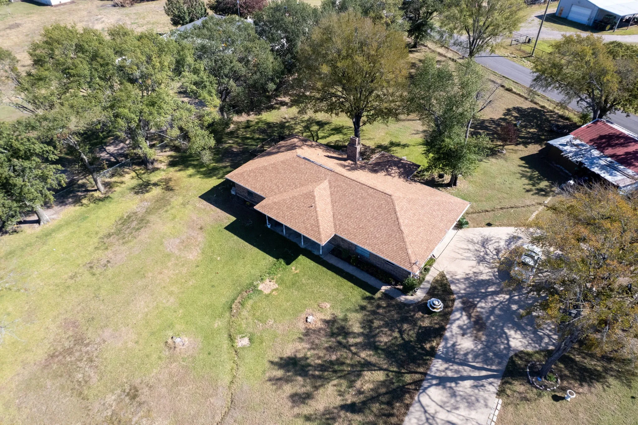 Expansive lot with mature trees, a driveway, and a residential structure featuring a shingle roof and a covered porch