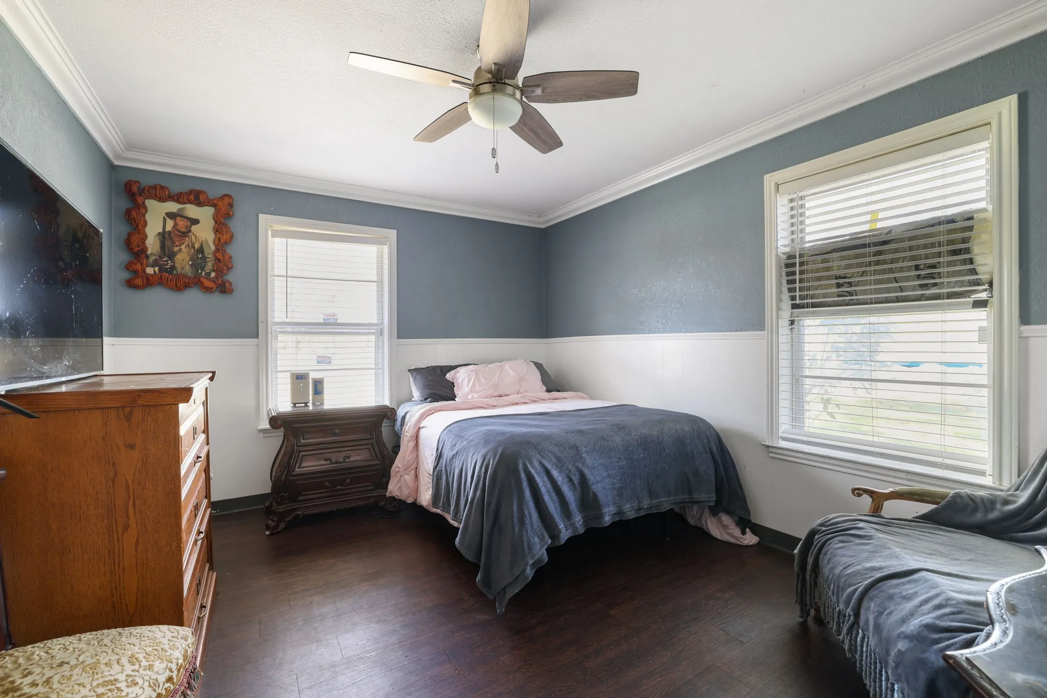 Wood-finish flooring, two windows with blinds, ceiling fan, and crown molding