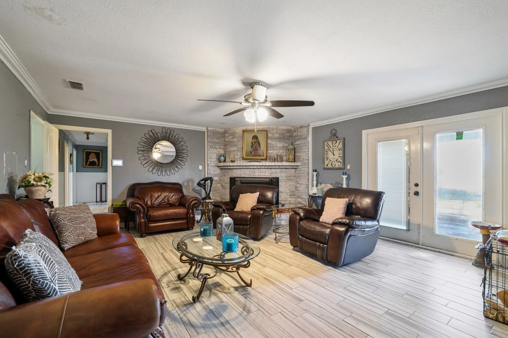 Living space featuring wood-finish flooring, a ceiling fan, crown molding, and a fireplace with a stone surround