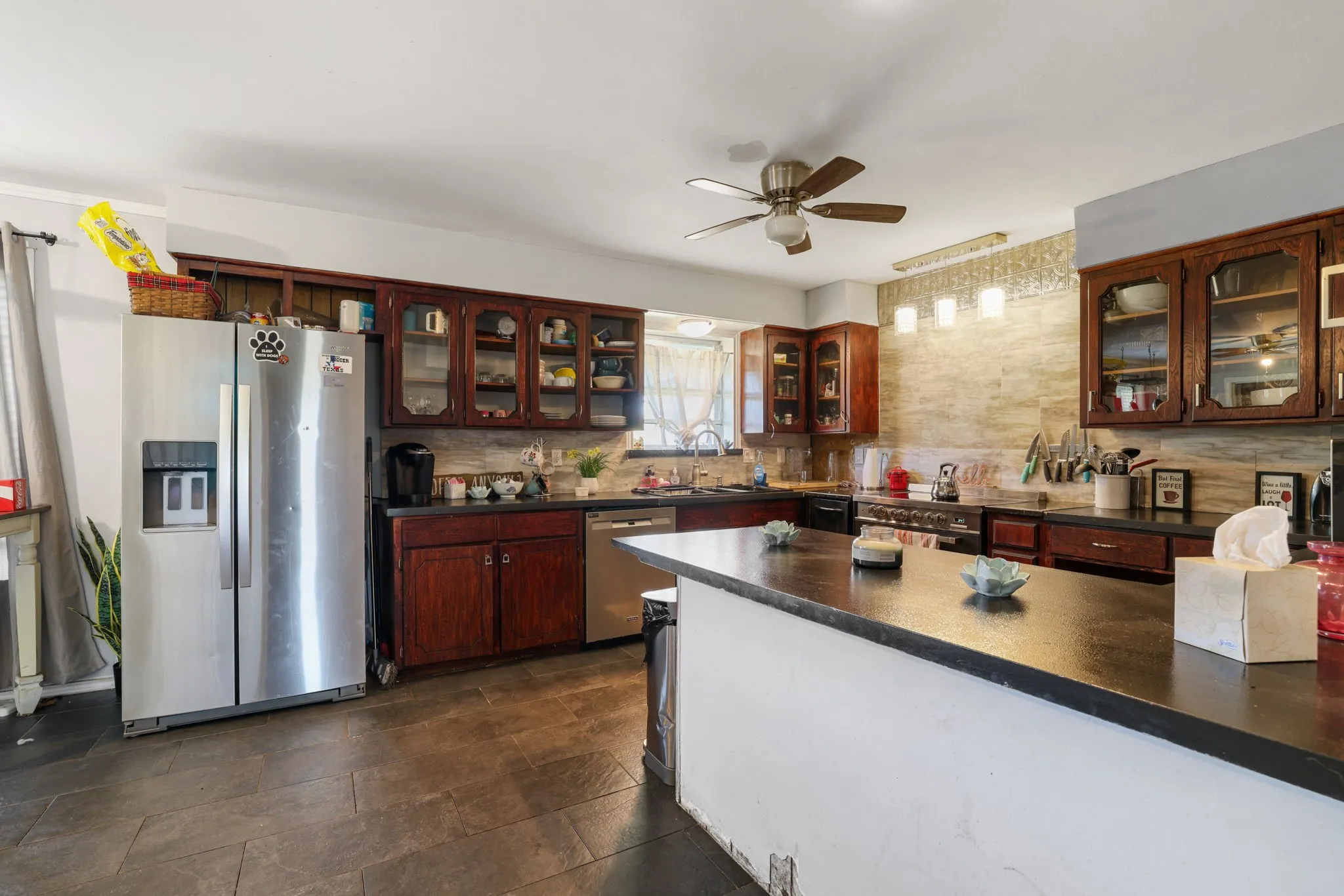 Kitchen featuring dark wood cabinetry, dark countertops, tiled flooring, and a ceiling fan