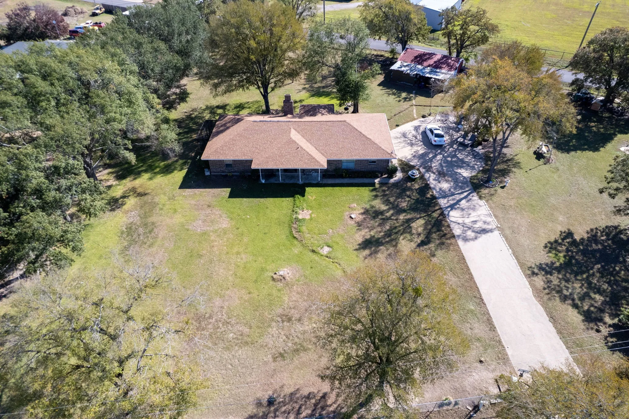 Expansive property featuring a single-story residence, a large driveway, mature trees, and a spacious green area