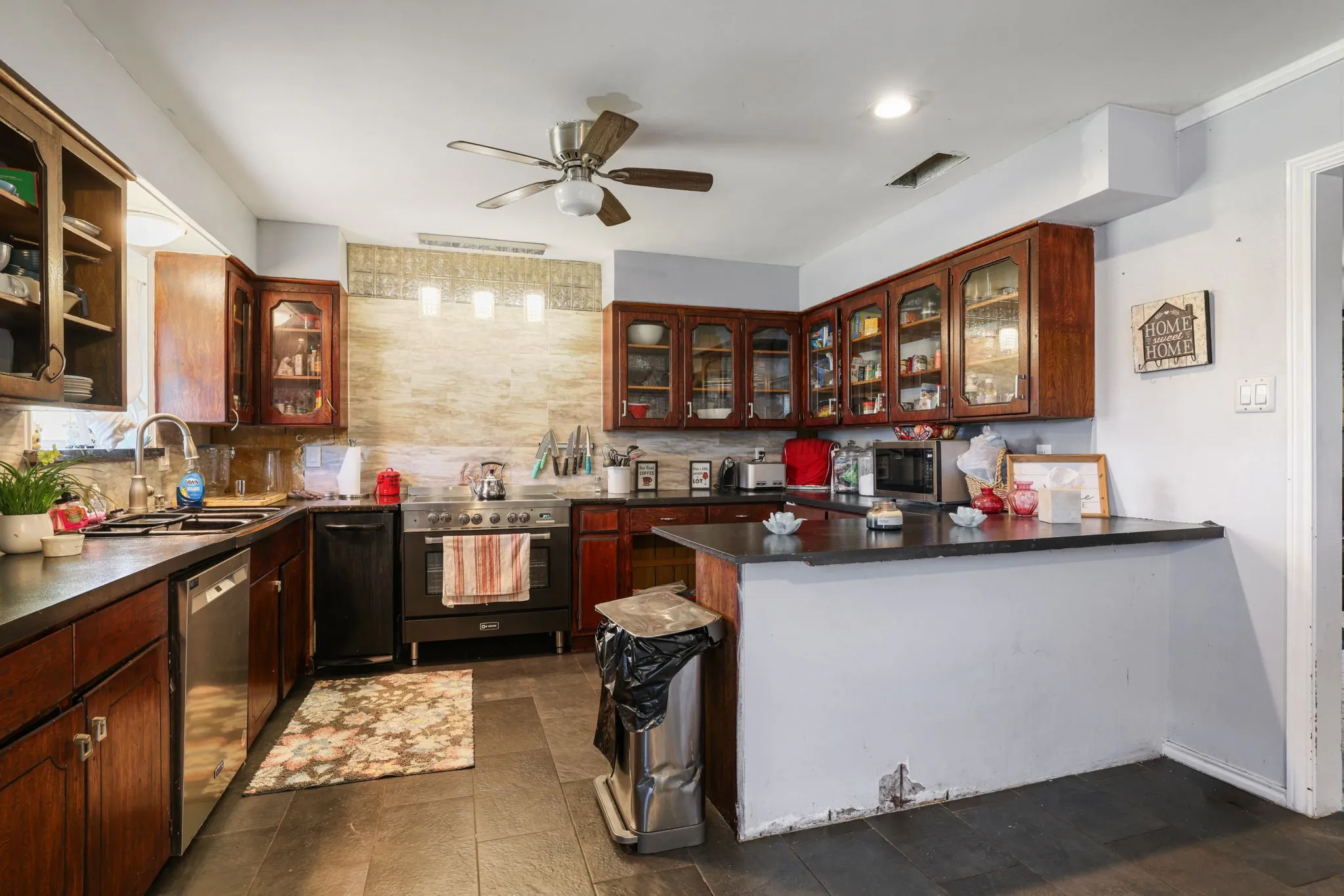 Kitchen featuring wood cabinetry, stainless steel dishwasher, tile flooring, built-in breakfast bar, and ceiling fan