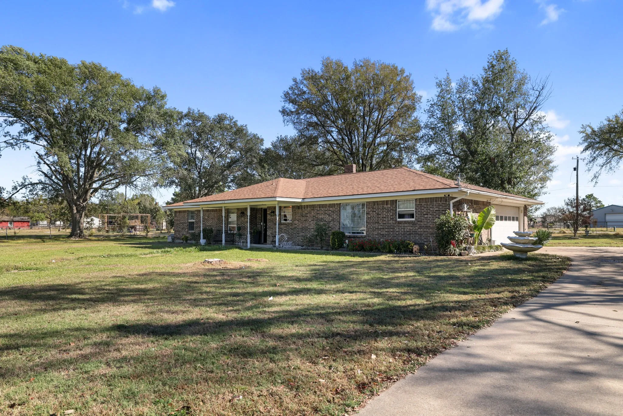 Brick exterior with a covered front porch, attached garage, concrete driveway, and mature trees