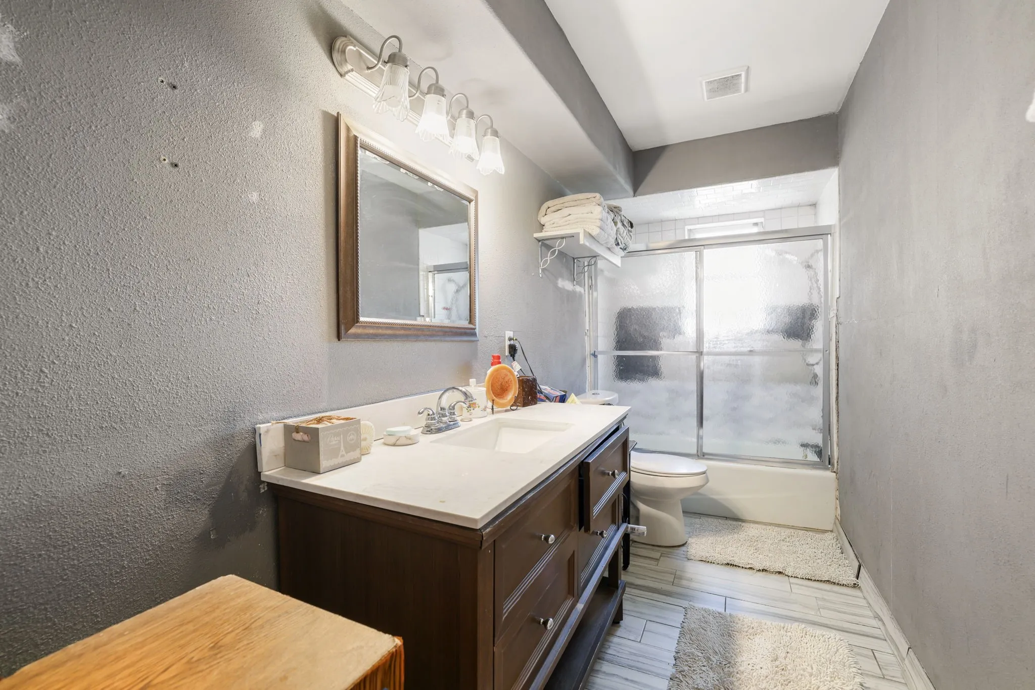Master bathroom featuring a dark wood vanity with dual sink configuration, white quartz countertop, framed mirror with sconce lighting, and an enclosed shower with sliding glass doors