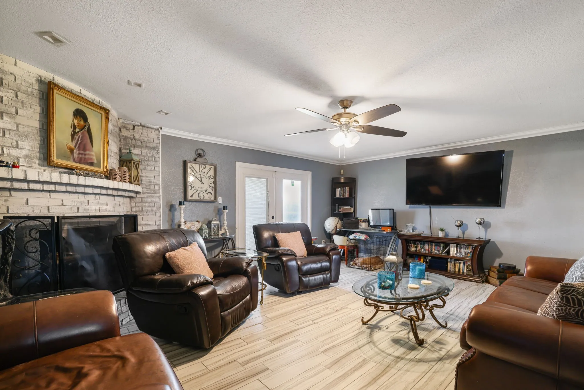 Living area with brick fireplace surround, light-toned wood-finish flooring, and crown molding