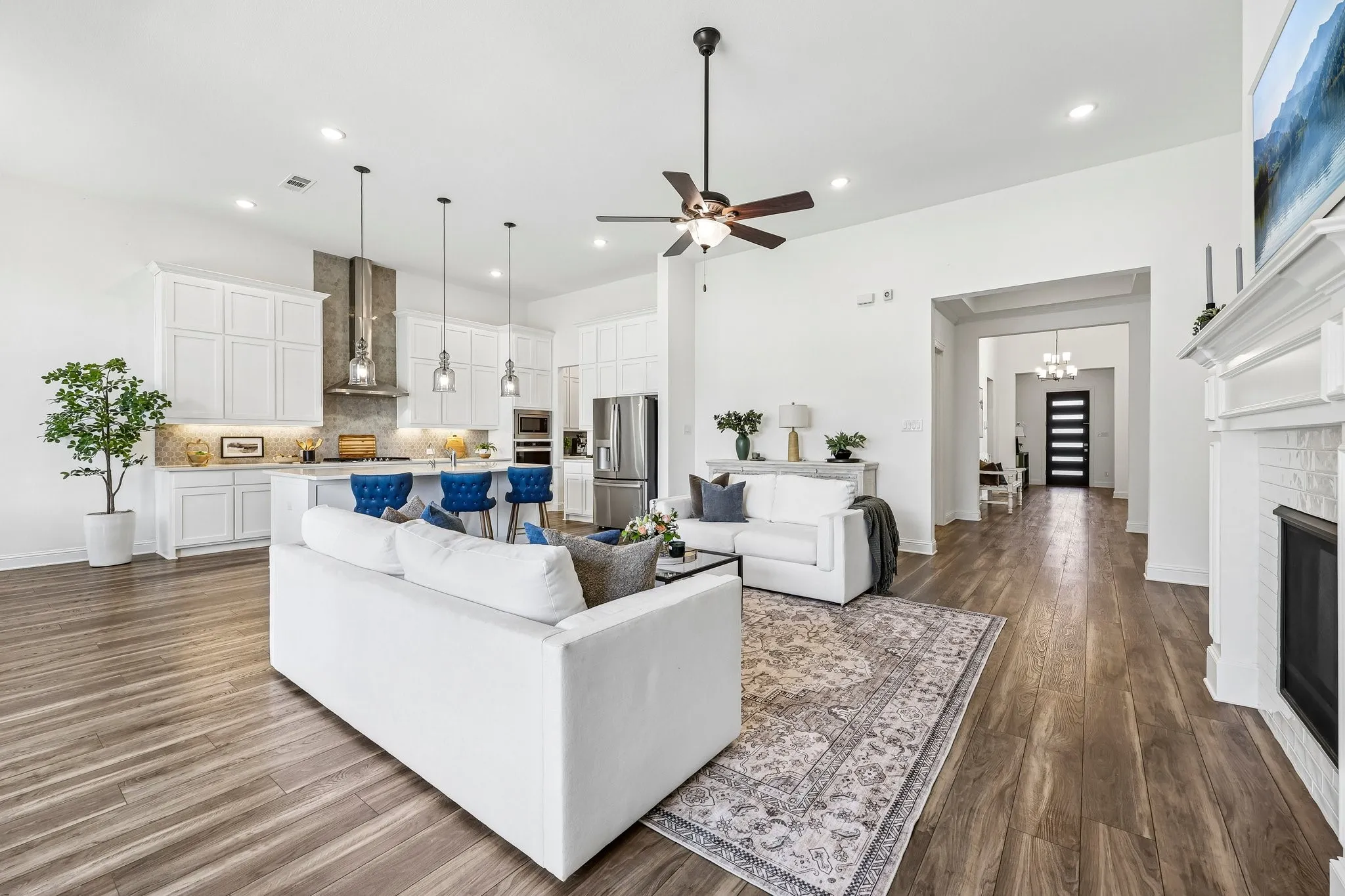 Open-concept living area featuring wood-finish flooring, a white-painted fireplace with a mantel, and a ceiling fan