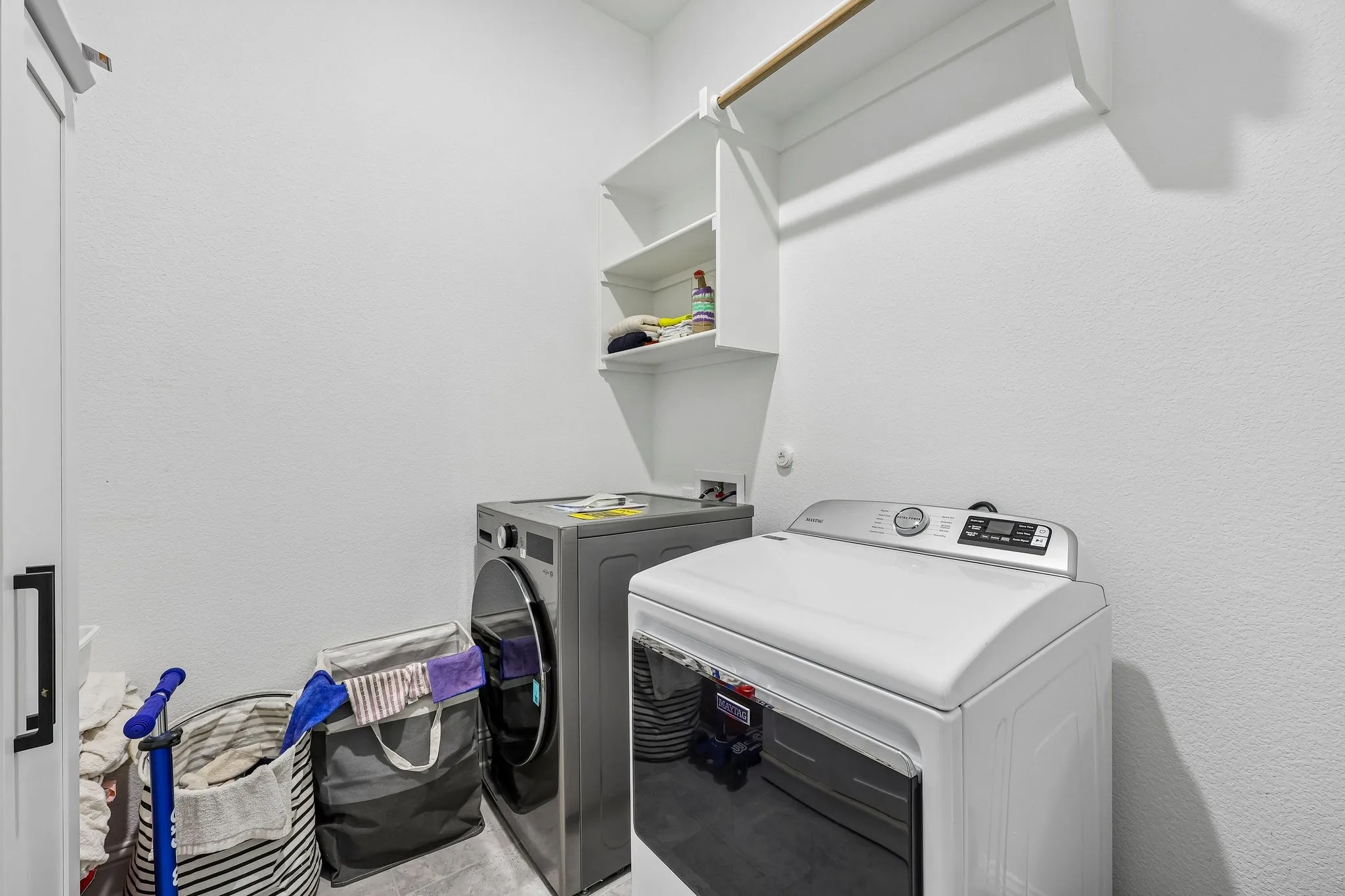 White laundry room featuring built-in shelving, a clothes hanging rod, and a closed-door cabinet
