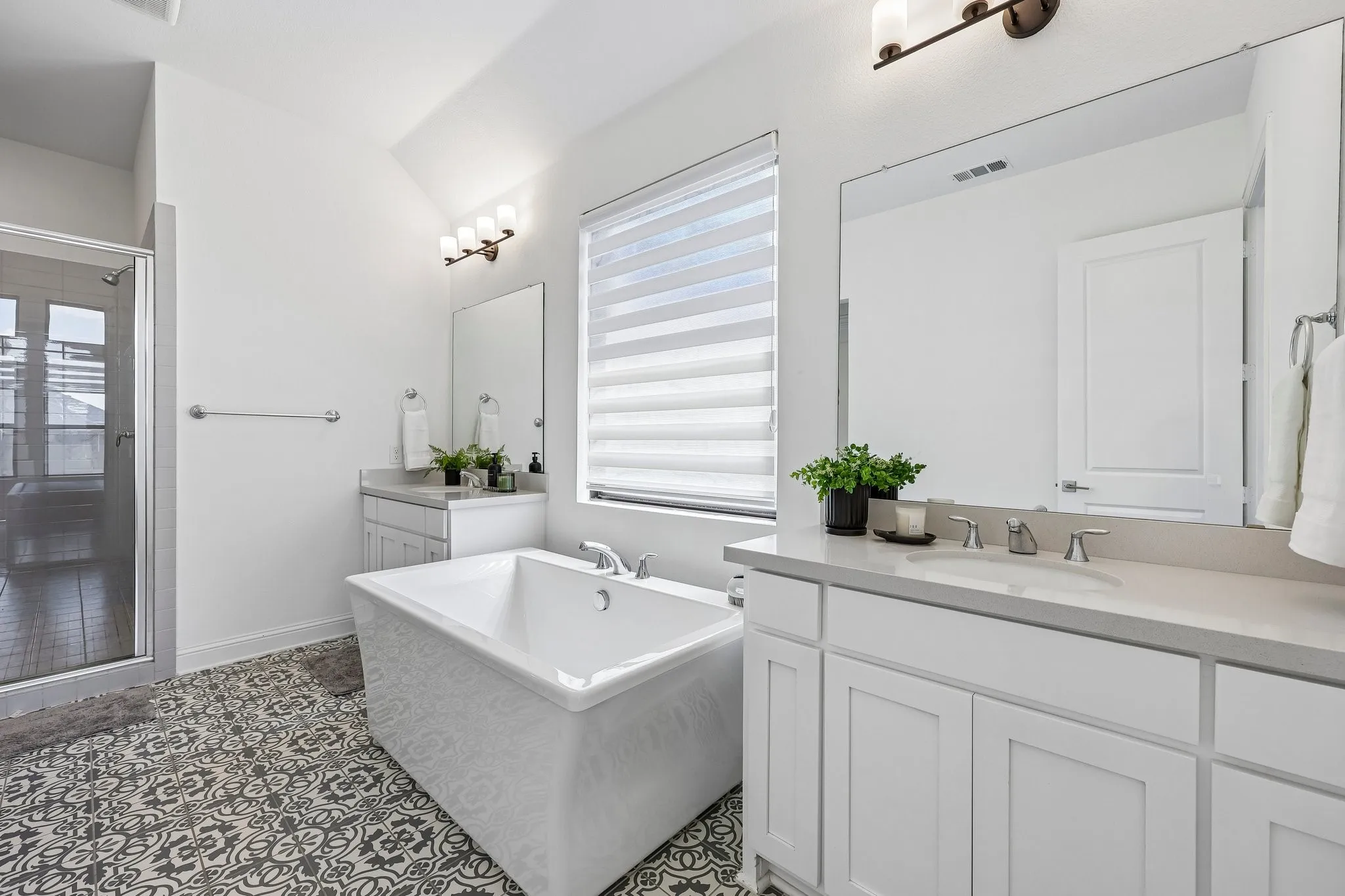 White walls with sloped ceilings, patterned floor tiles, a freestanding soaking tub, dual vanities with integrated sinks, and a glass-enclosed shower
