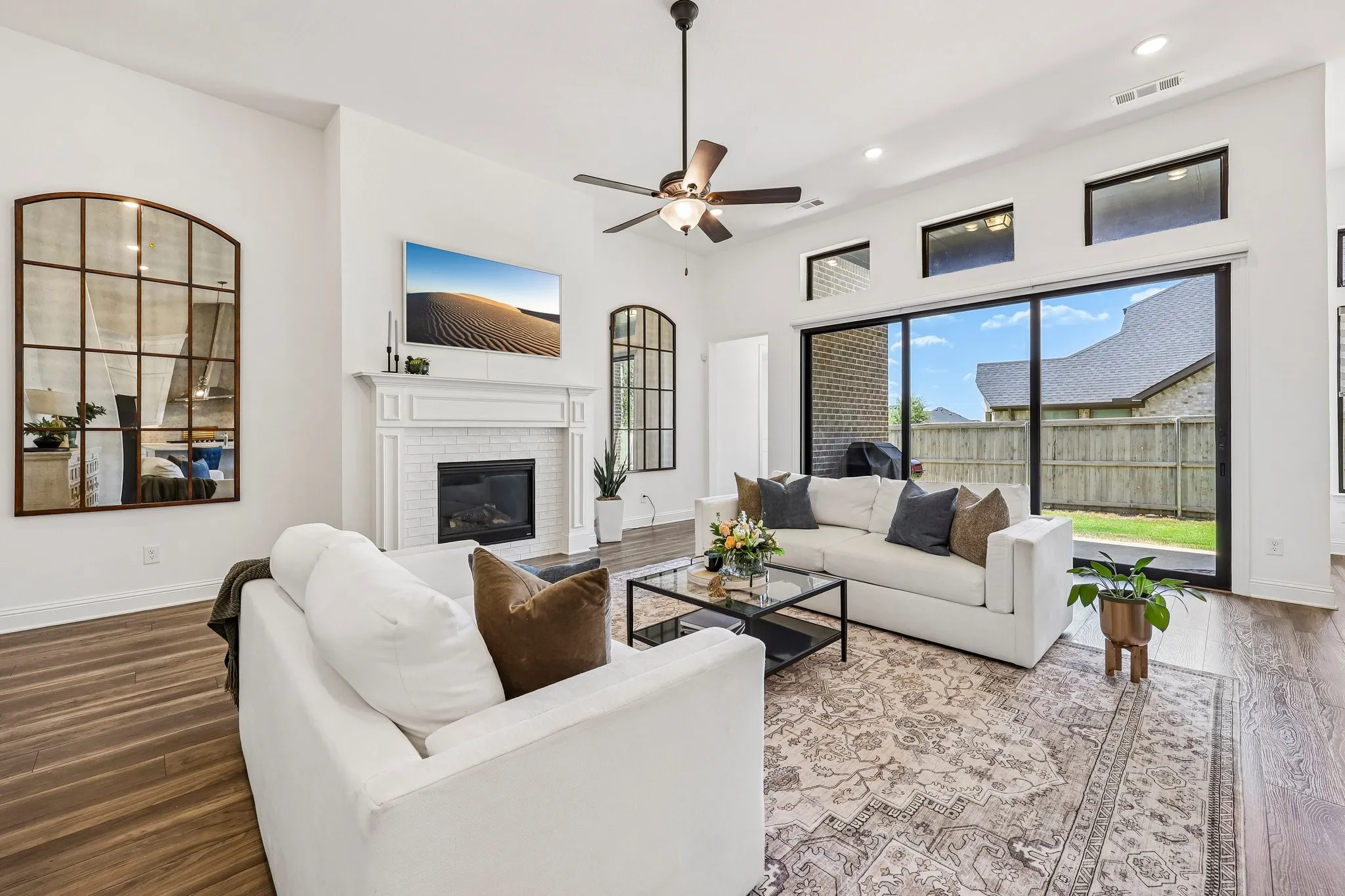 High ceilings with recessed lighting, wood-finish flooring, a white brick fireplace with a mantel, and an expansive sliding glass door to the exterior