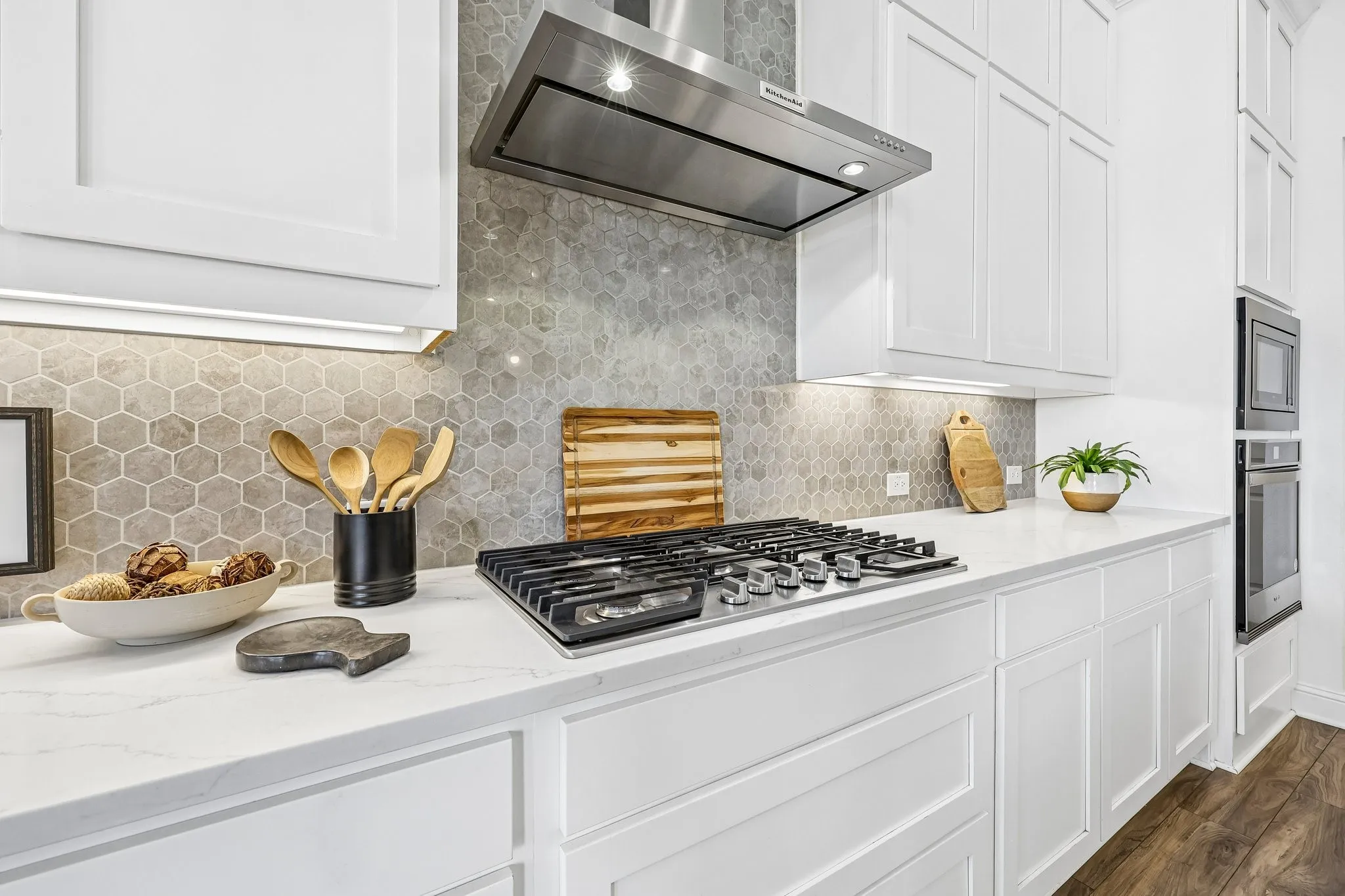 White shaker cabinetry, honeycomb tile backsplash, stainless steel gas range, built-in stainless steel appliances, and under-cabinet lighting