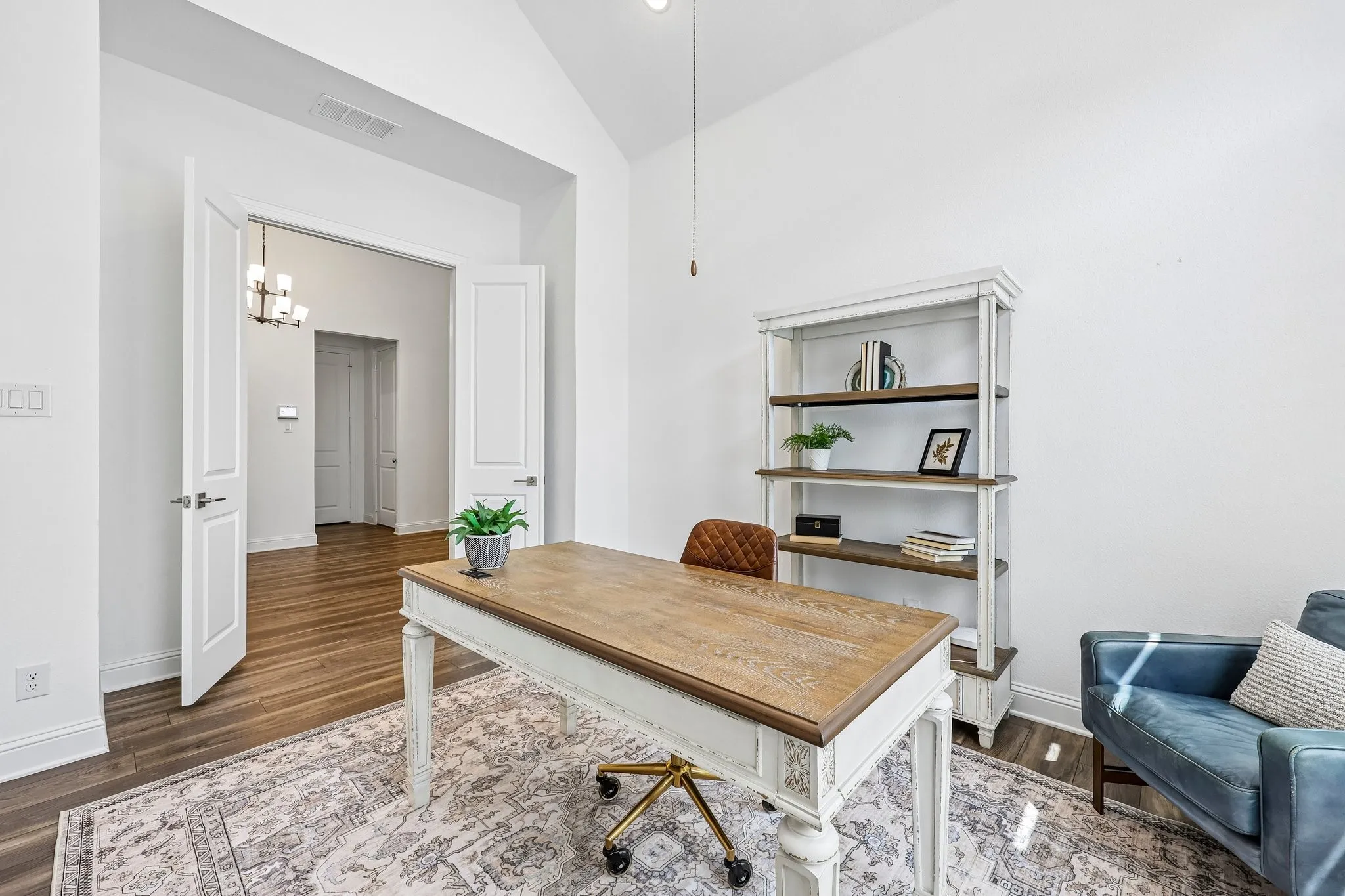 Vaulted ceiling with recessed lighting, wood-finish flooring, double doors with paneled design, and a modern chandelier in the adjacent space