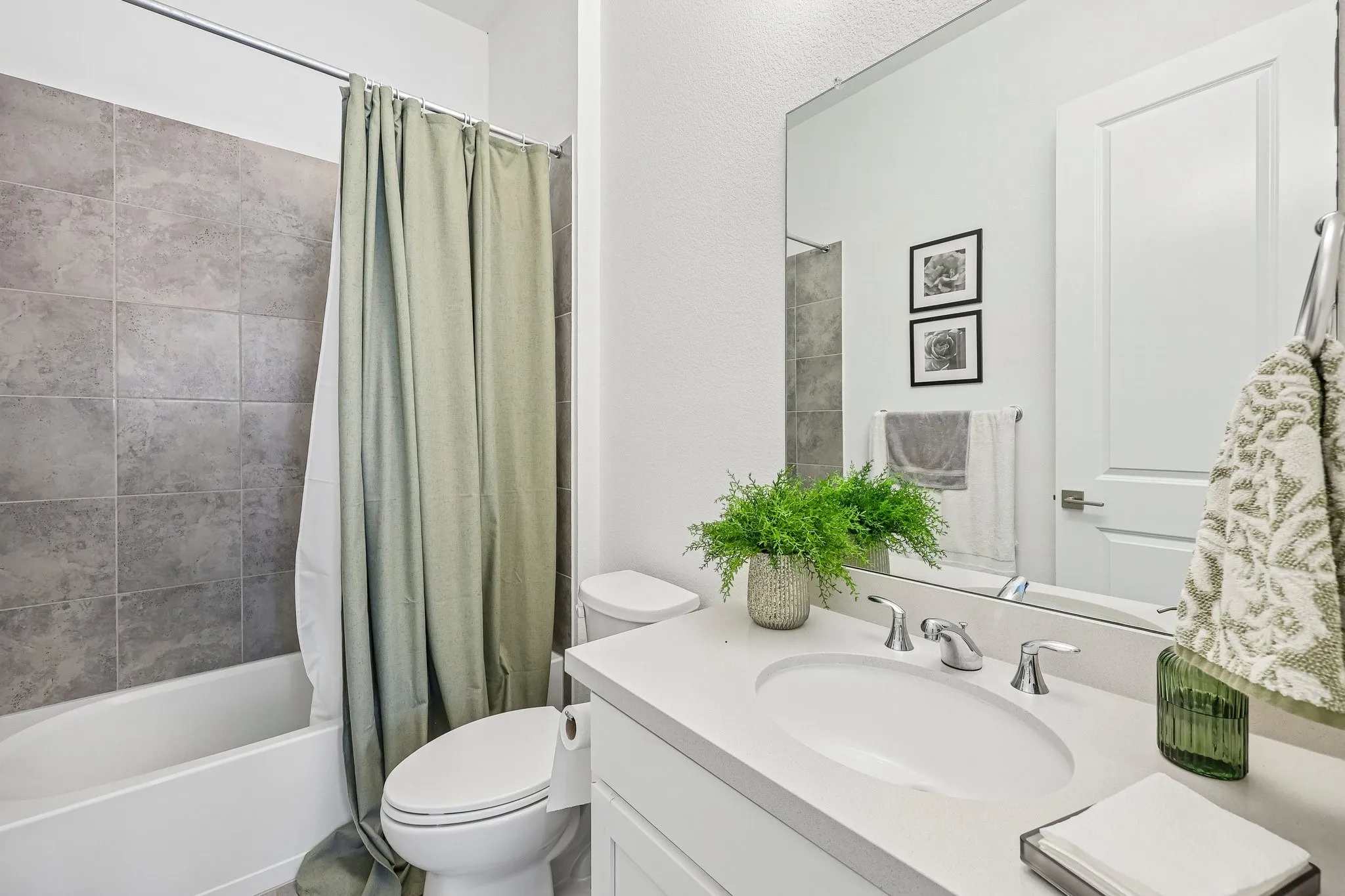 Contemporary bathroom featuring a single vanity with an integrated sink, a large mirror, a toilet, and a shower-over-tub combination with tile surround