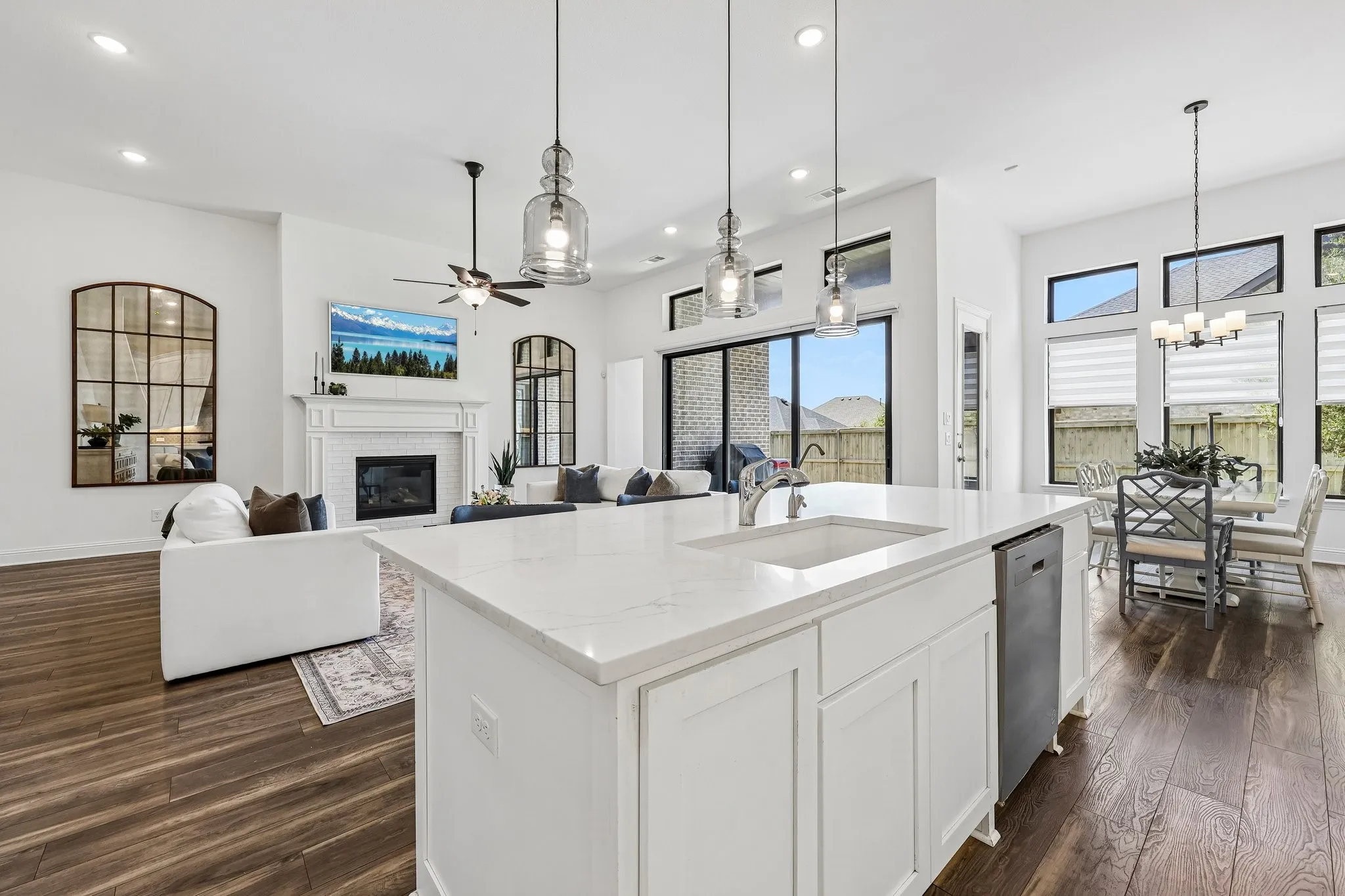 Open-concept living space featuring wood-finish flooring, a kitchen island with a built-in sink, and pendant lighting