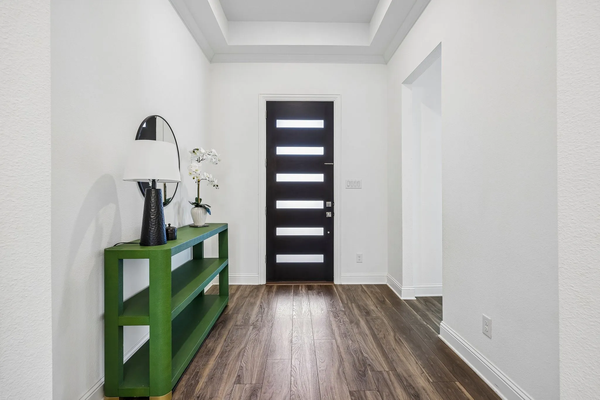 Tray ceiling, wood-finish flooring, white walls, and a black entryway door with frosted glass panels