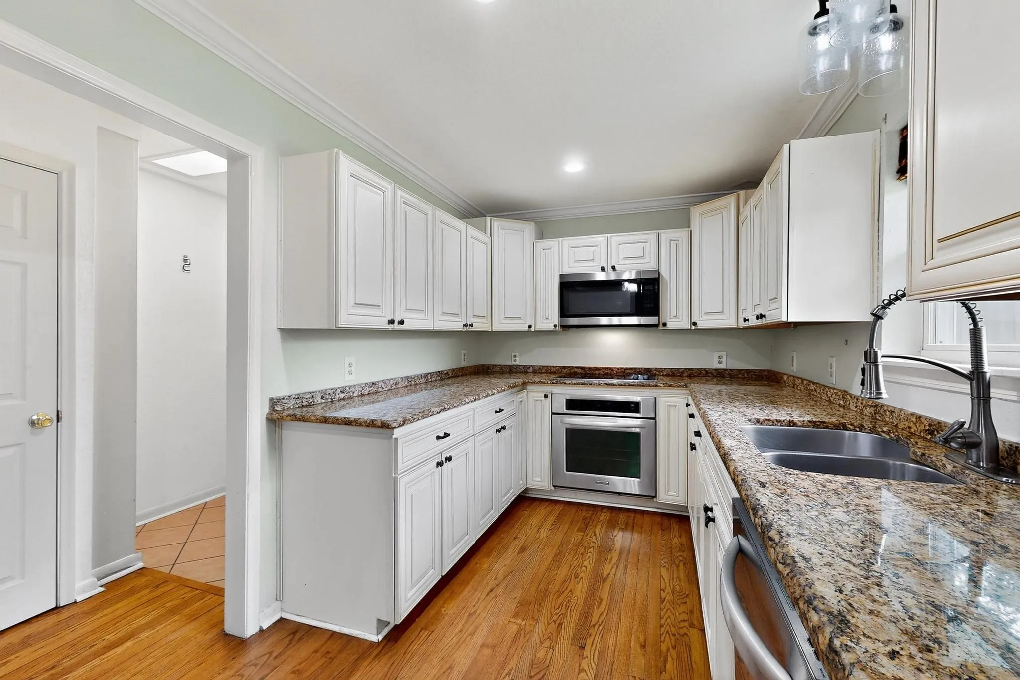 Kitchen with appliances with stainless steel finishes, white cabinetry, crown molding, stone counters, and light wood-style floors