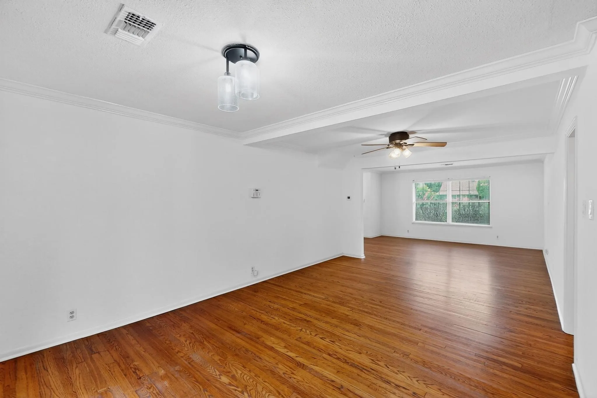 Empty room with wood finished floors, a textured ceiling, a ceiling fan, and crown molding