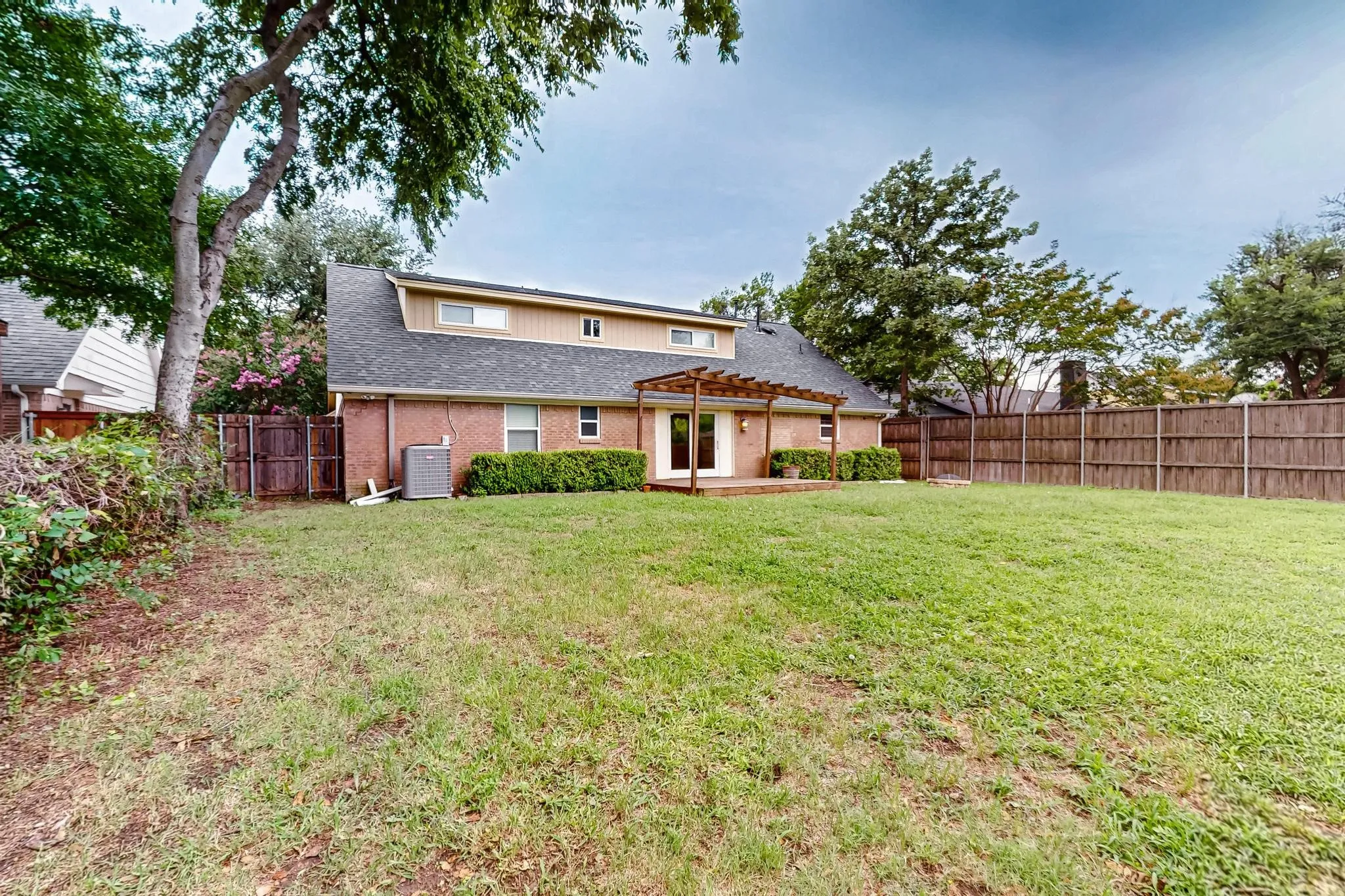 Rear view of house featuring a pergola, a fenced backyard, brick siding, roof with shingles, and a patio