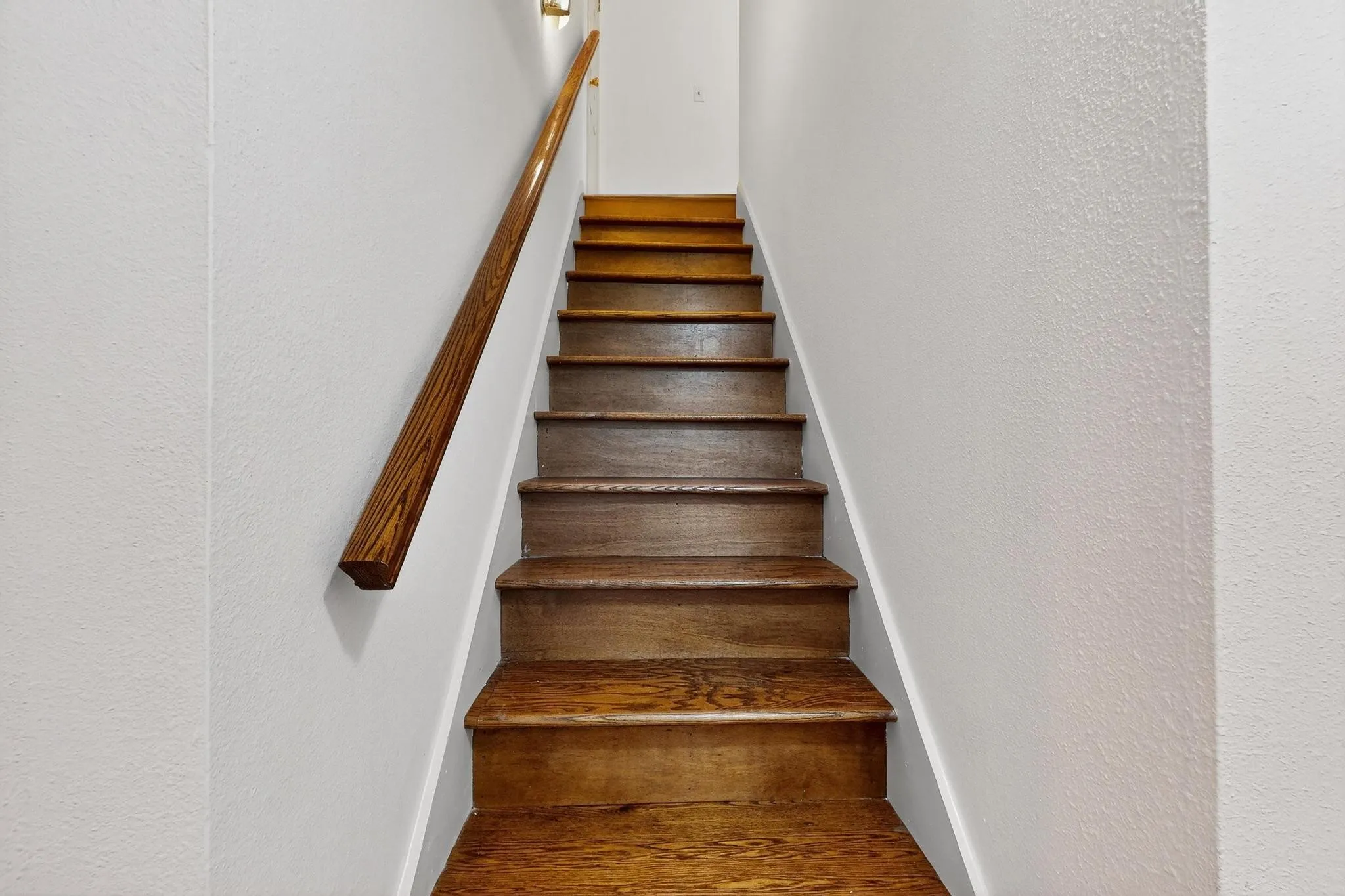 Stairway featuring wood finished floors and a textured wall