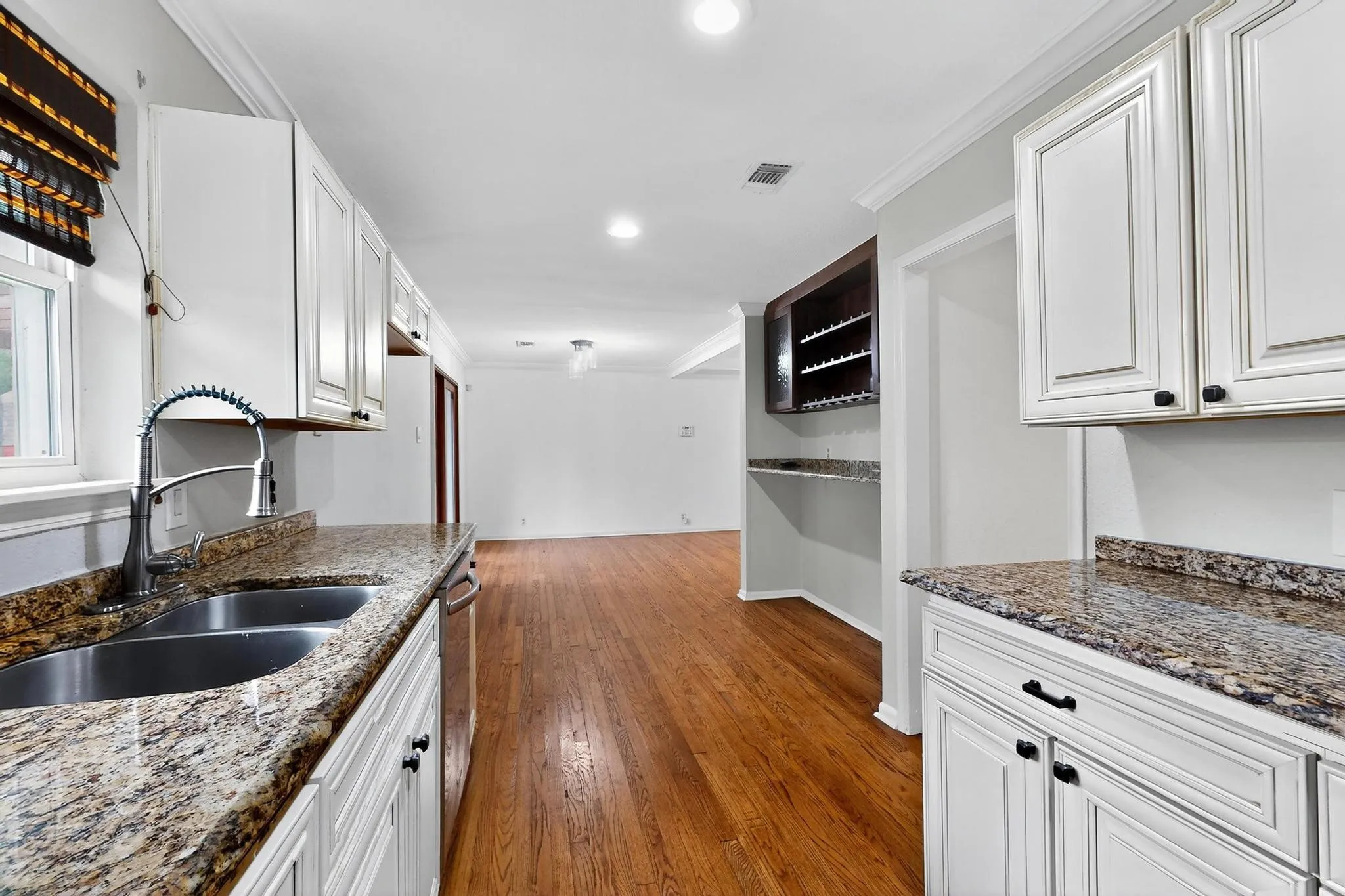 Kitchen with wood finished floors, crown molding, white cabinets, dark stone counters, and recessed lighting