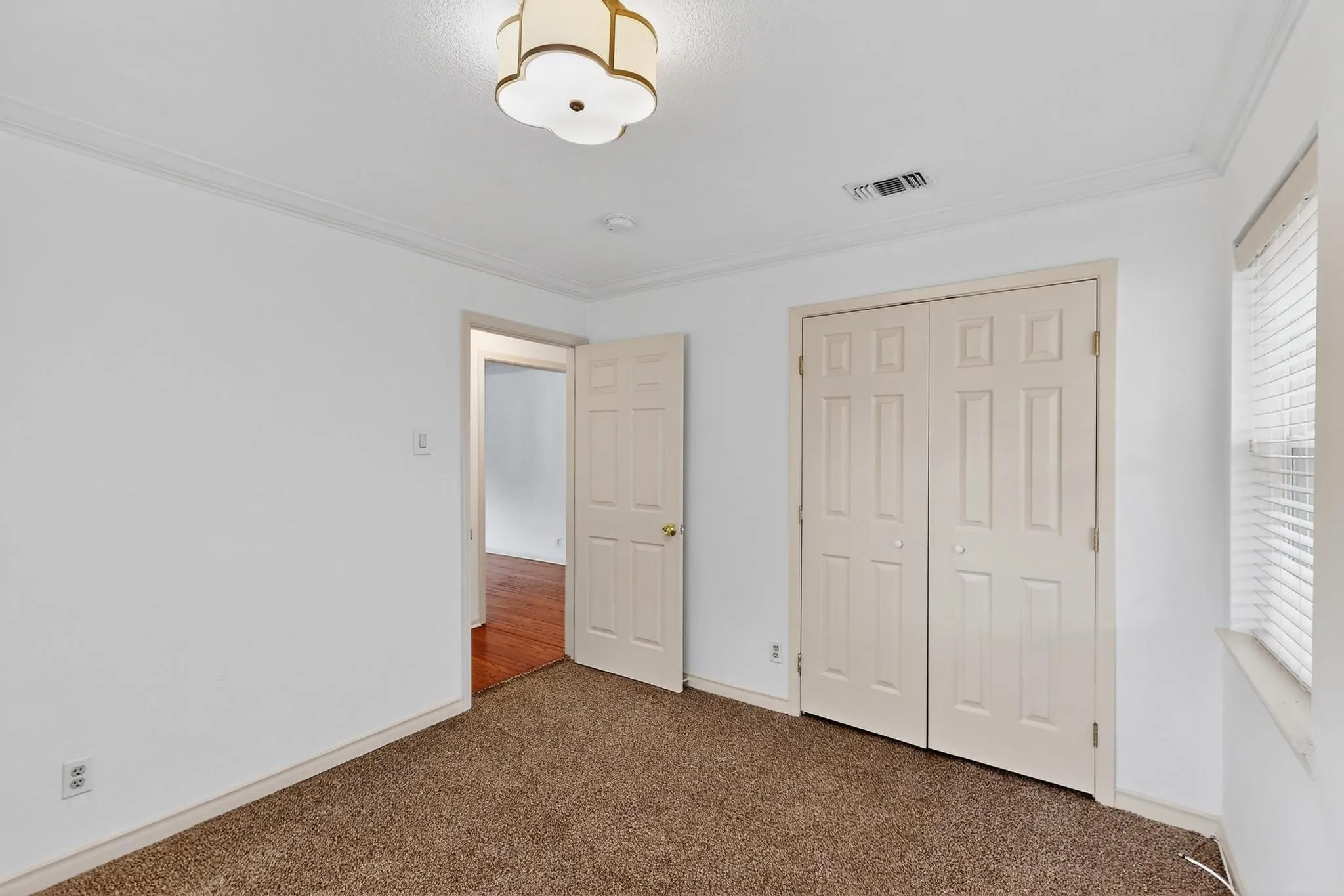 Unfurnished bedroom with carpet flooring, crown molding, a closet, and multiple windows